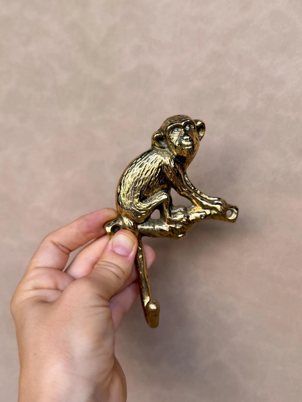 Detailed face and body of the brass monkey wall hook, held between two fingers
