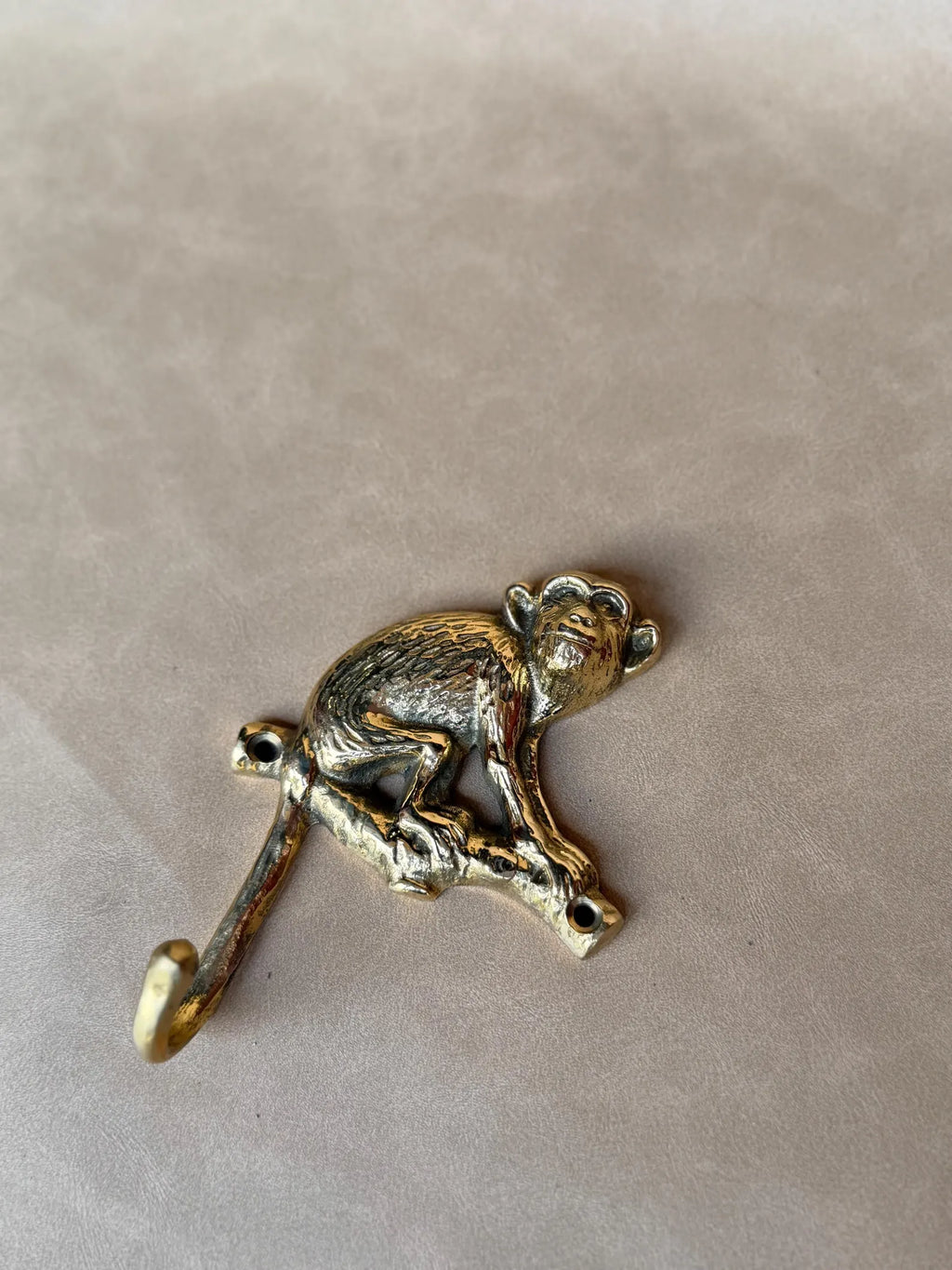 Brass monkey wall hook lying flat on a grey surface, top view