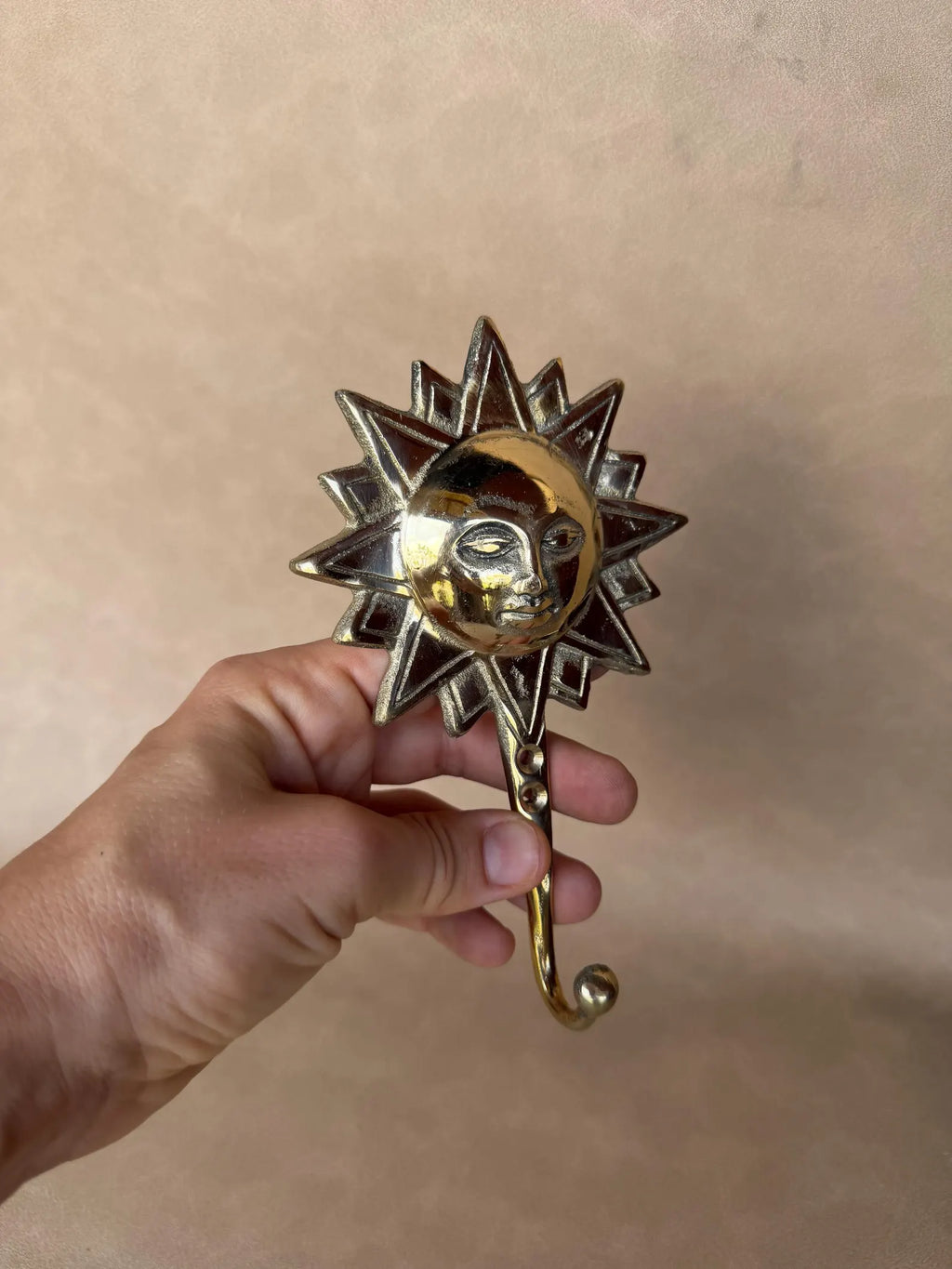 Hand holding the celestial brass sun hook with the hook pointing down
