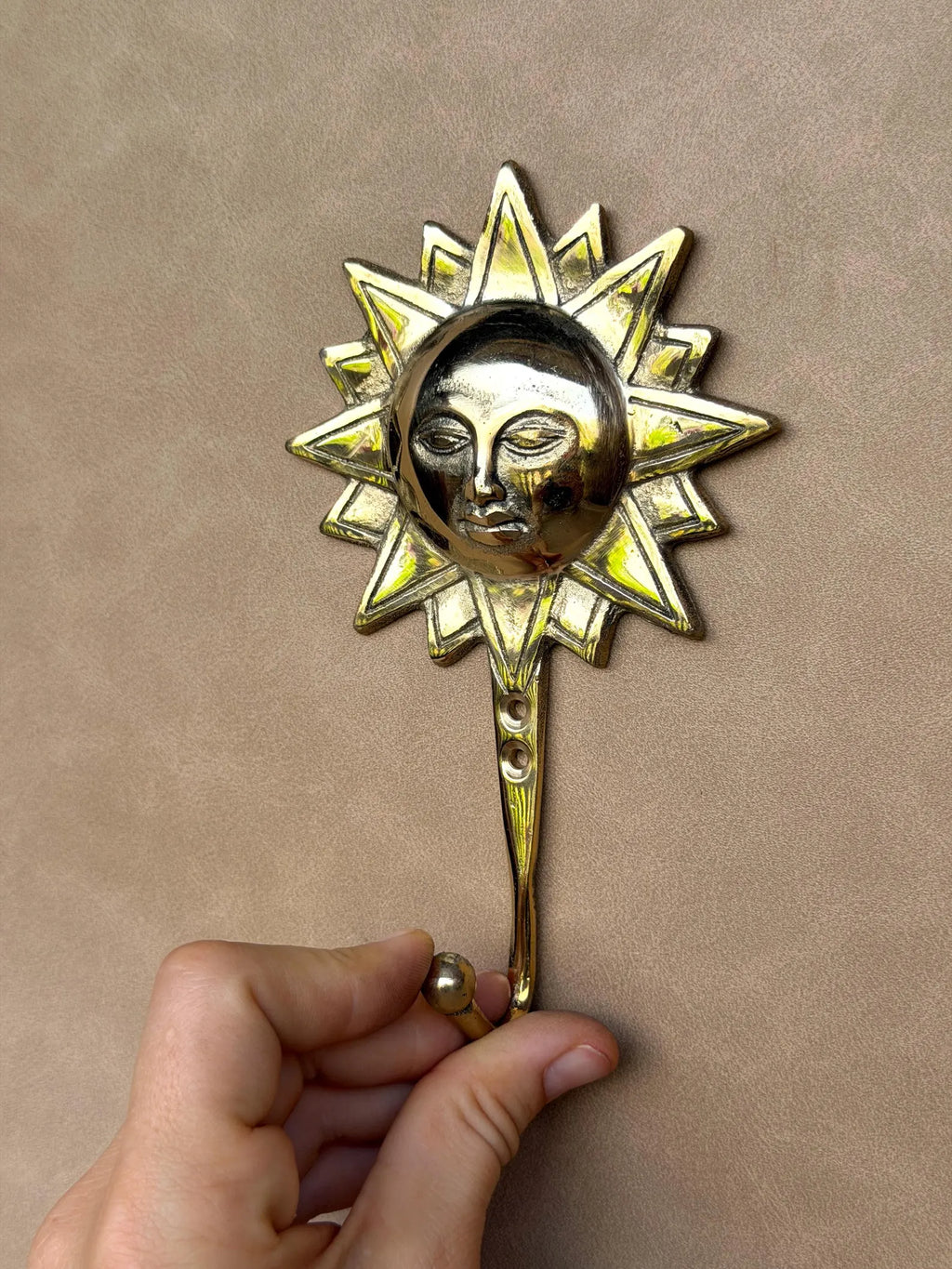 Hand holding the gold brass sun hook upright by its curved hook, full length view
