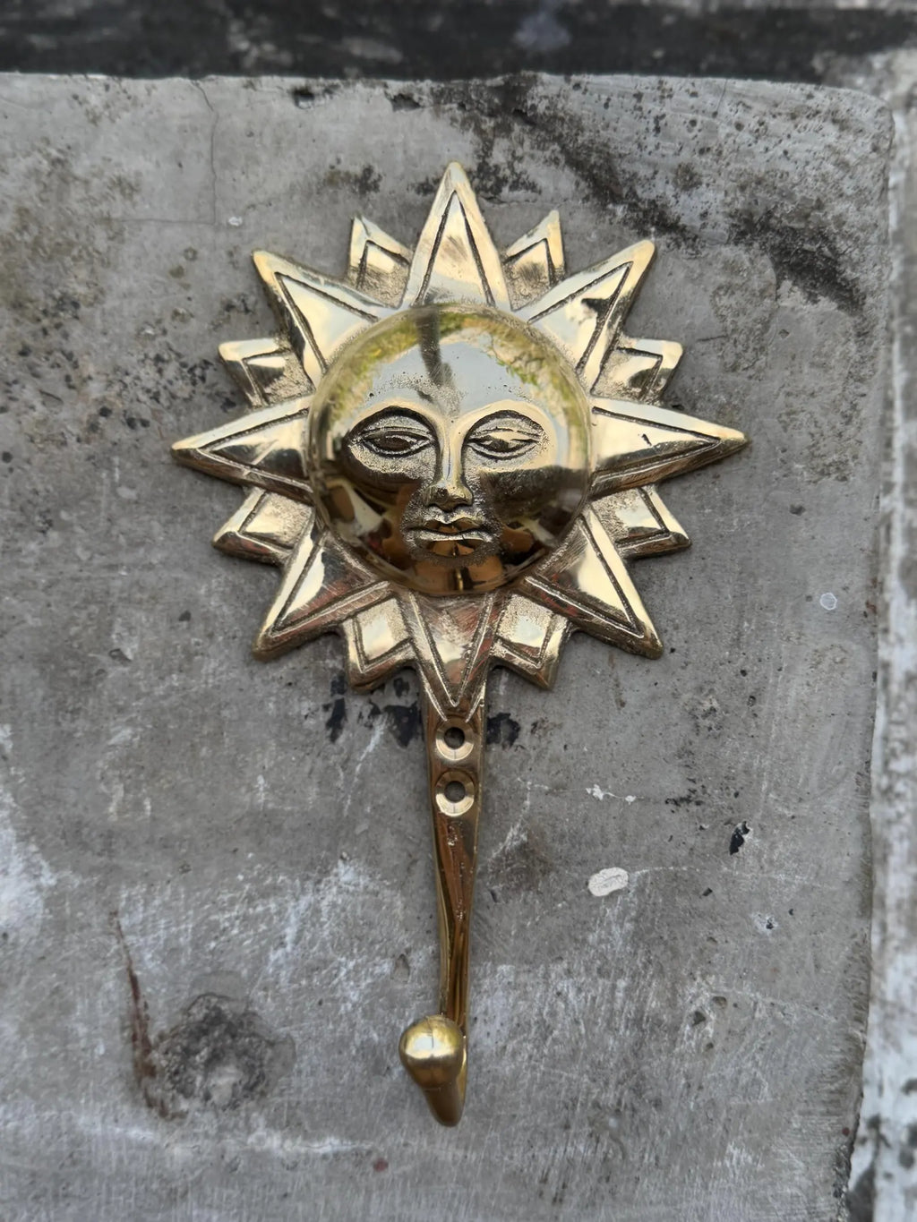 Front view of the brass sun face wall hook on a grey concrete background
