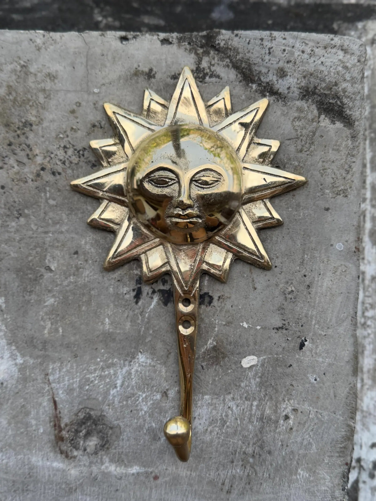 Front view of the brass sun face wall hook on a grey concrete background