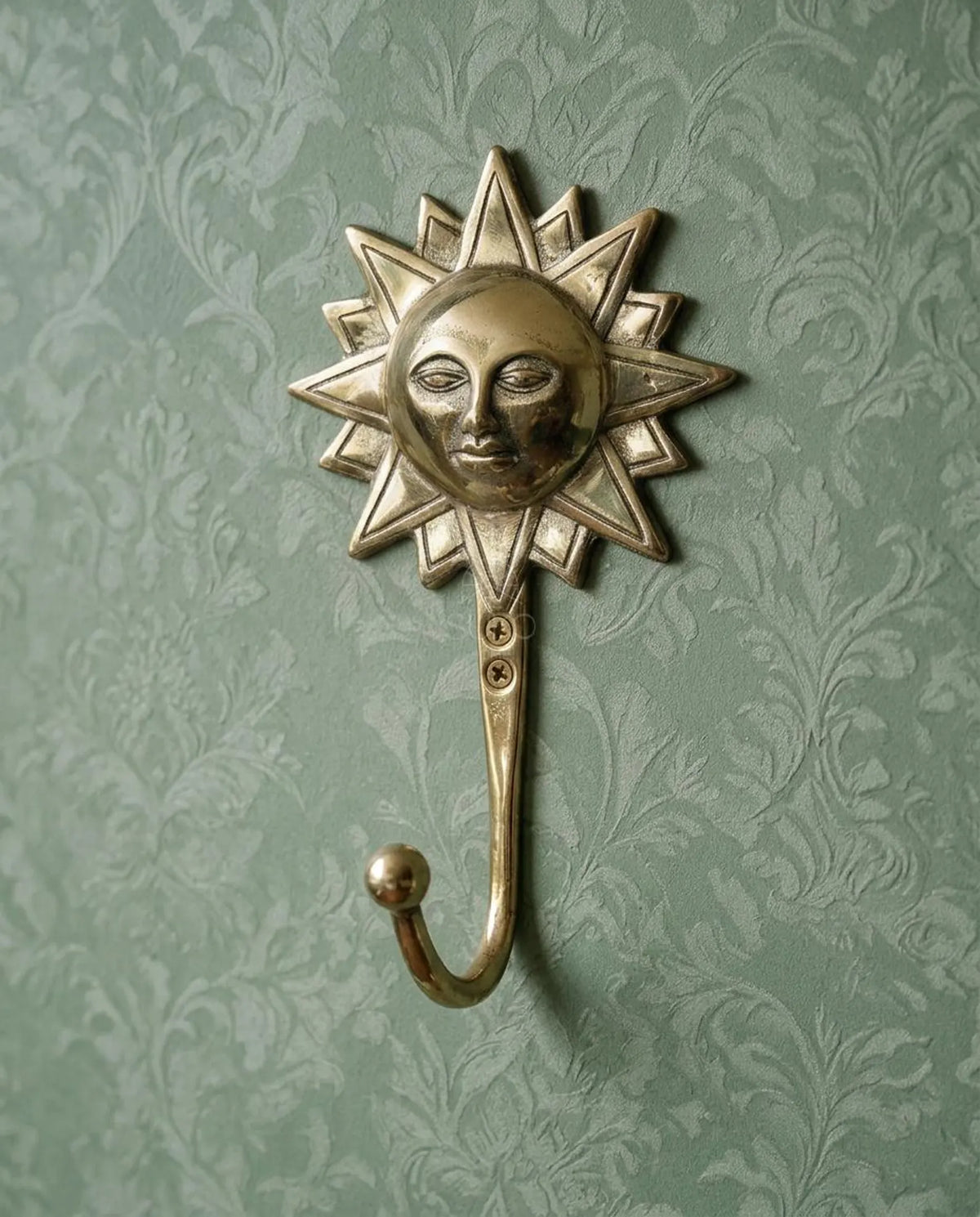 Brass sun face wall hook with radiant rays on green damask wallpaper