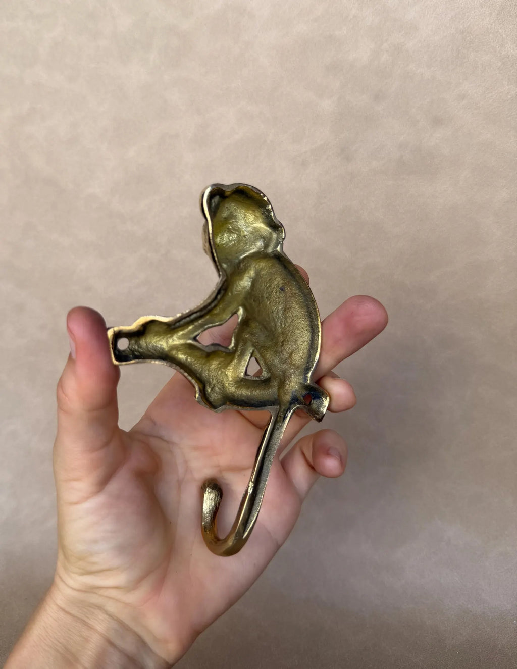 Brass monkey hook resting on an open palm to show its compact size