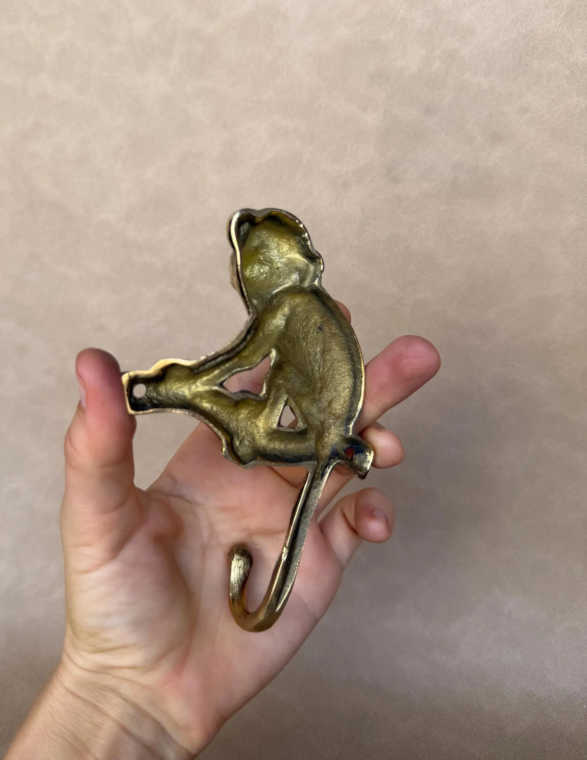Brass monkey hook resting on an open palm to show its compact size
