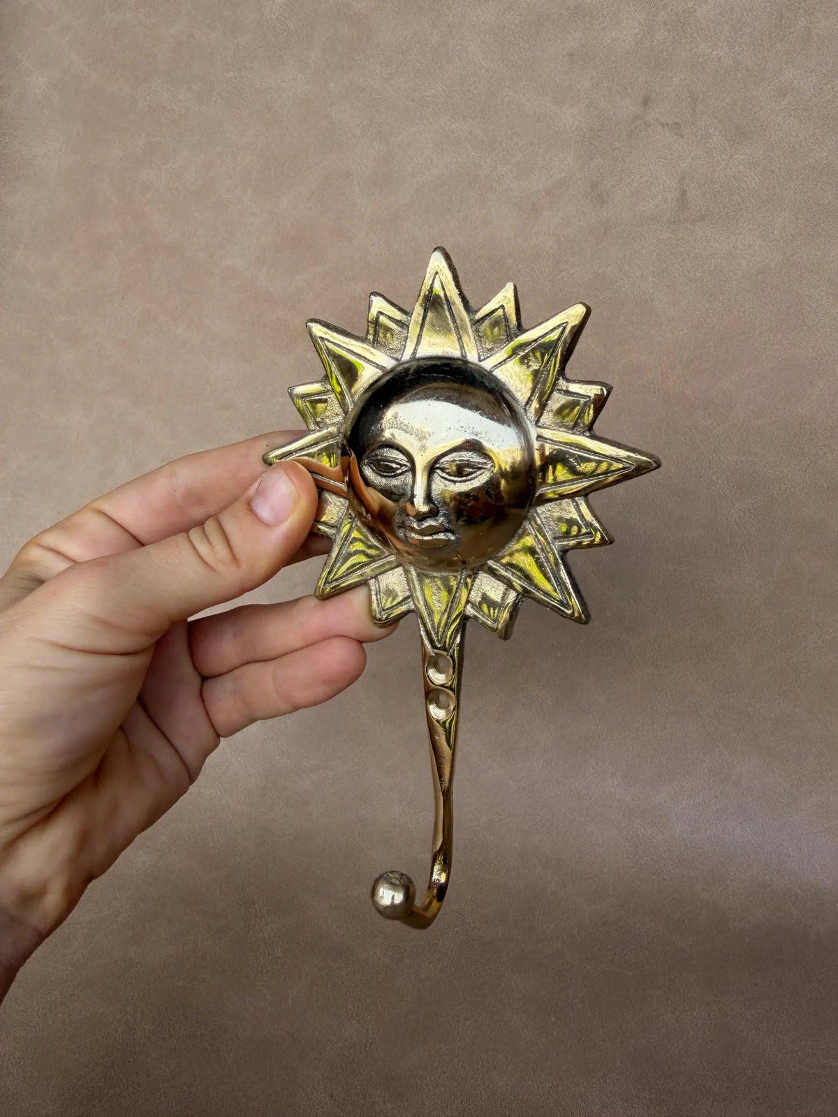 Sculpted sun face with pointed rays on a gold brass wall hook, held in hand