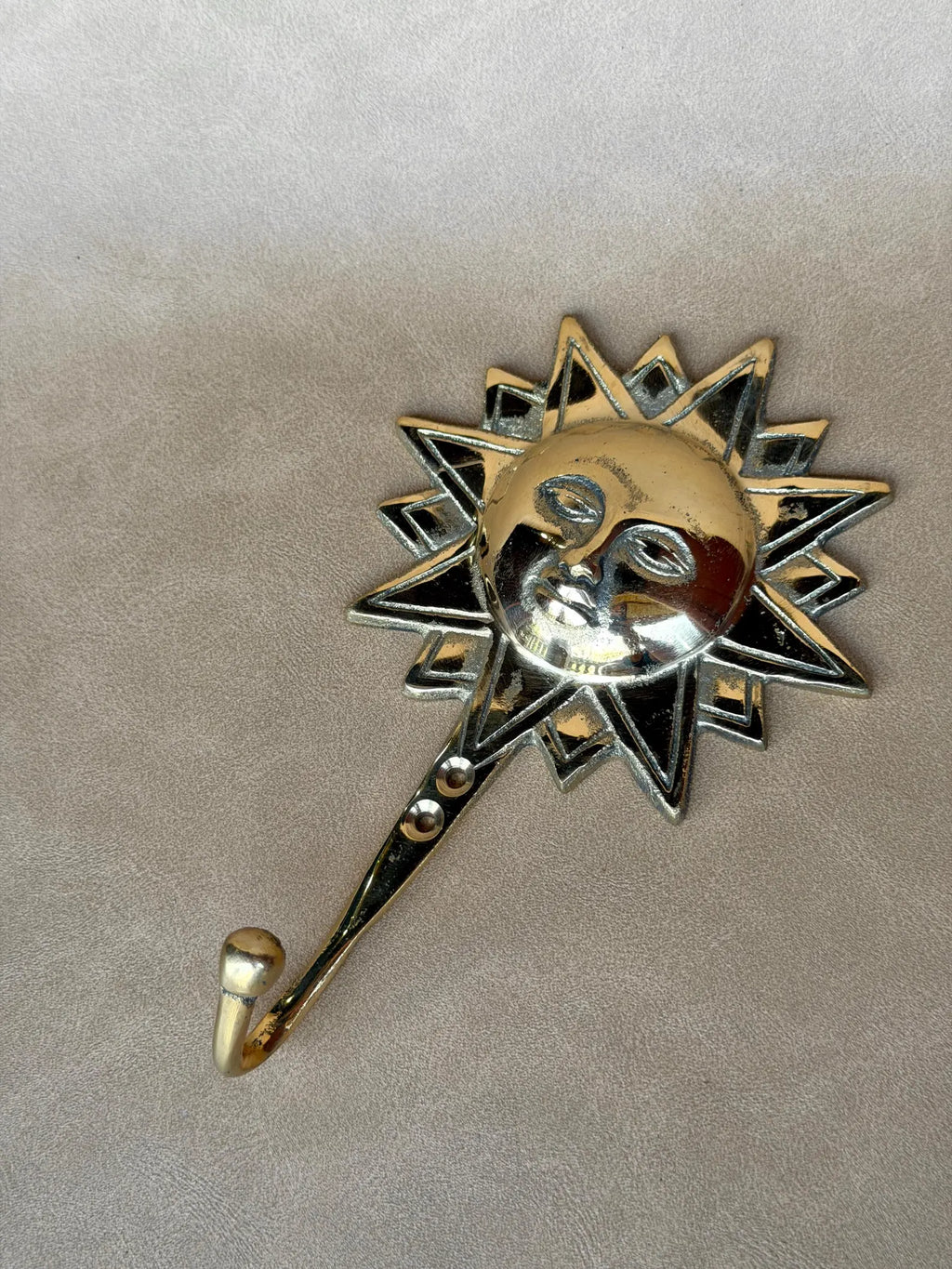 Brass sun face wall hook lying flat on a grey surface, top view