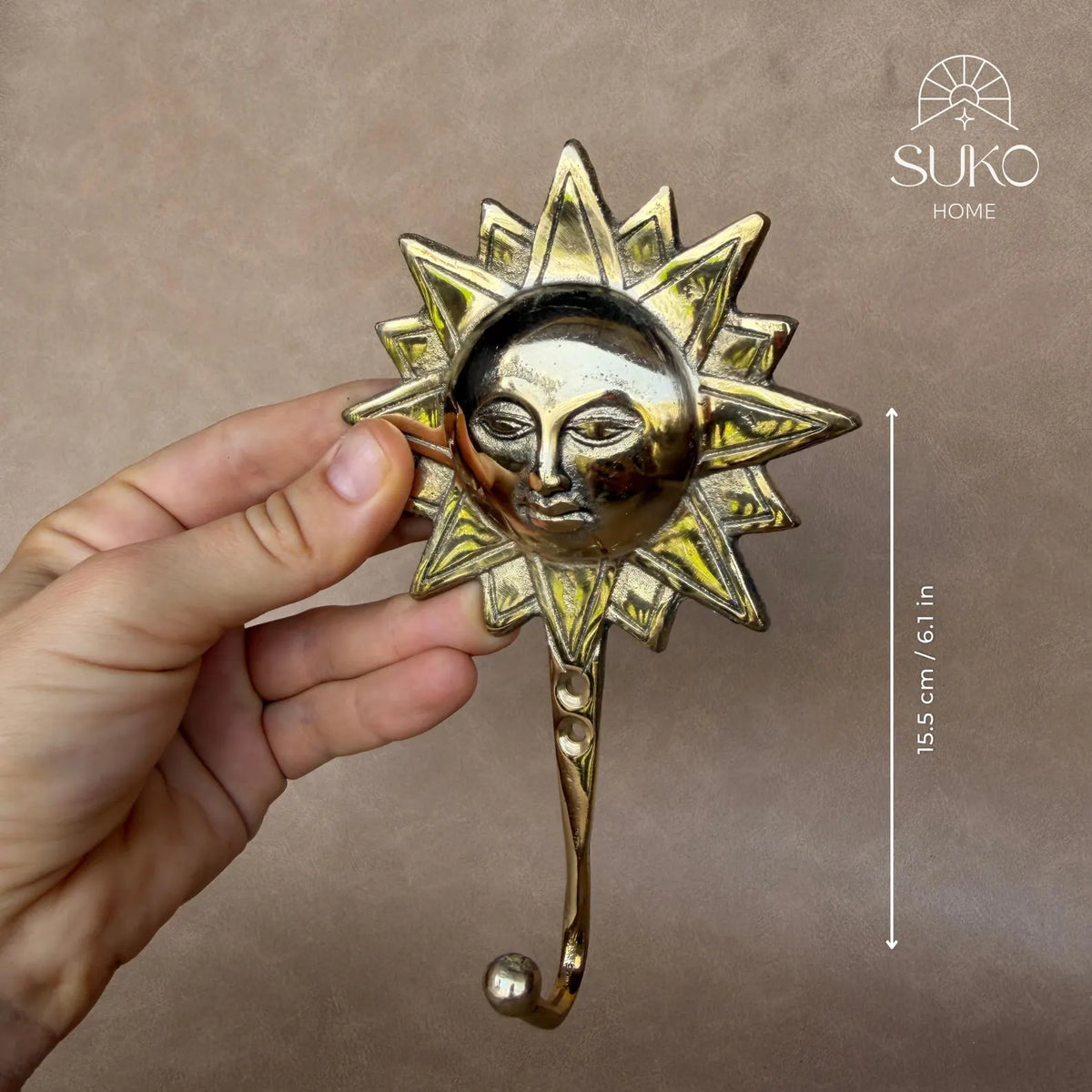 Hand holding the brass sun face hook with a size marker showing its length