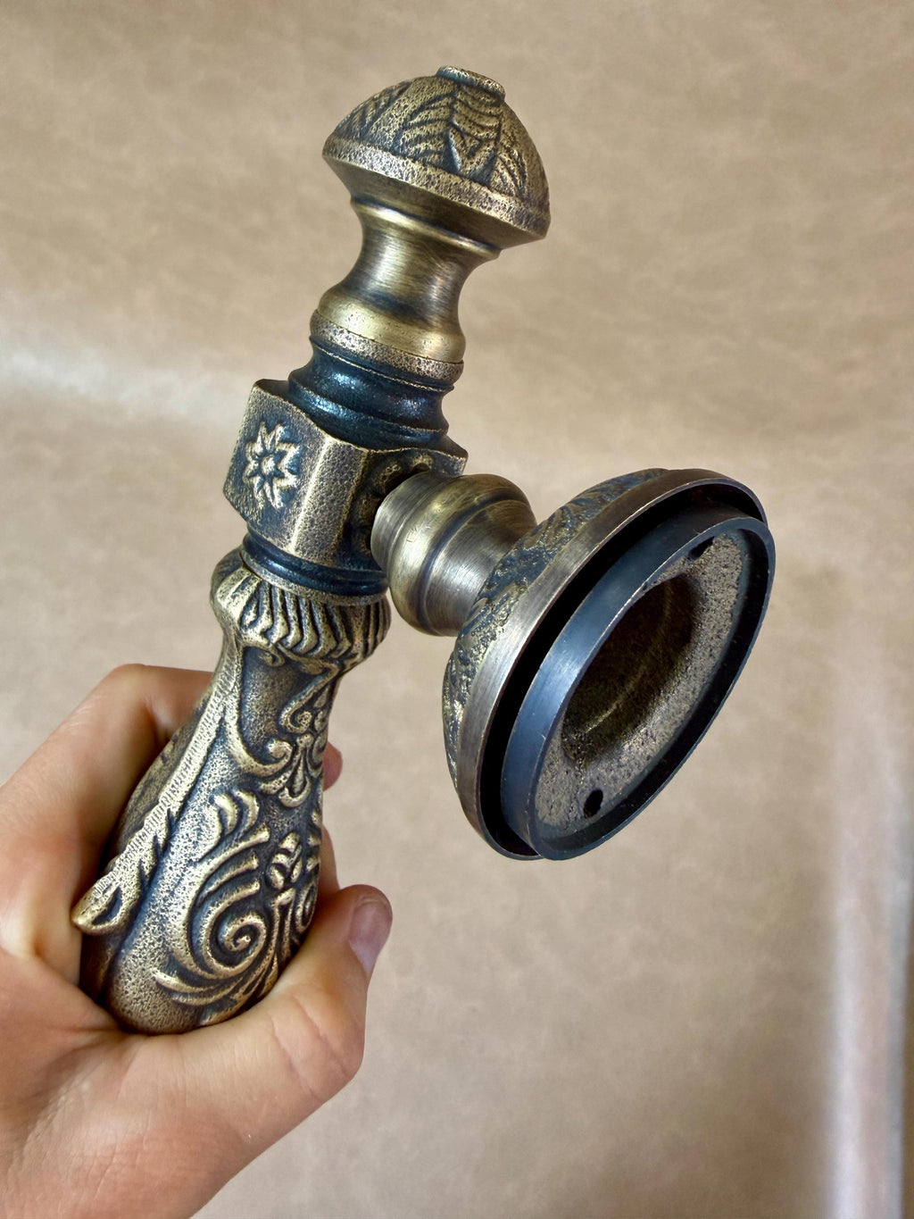Elongated grip and rounded finial of the ornate brass door pull, with a rubber gasket under the base