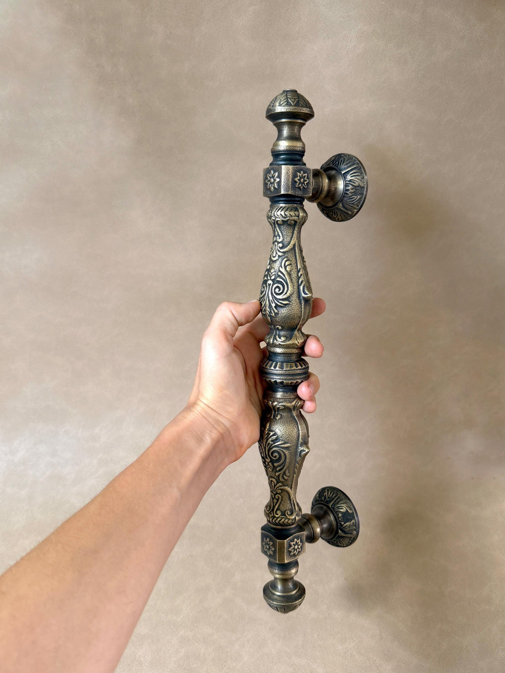 Long ornate antique brass door pull with embossed floral scrollwork and two round mounting plates