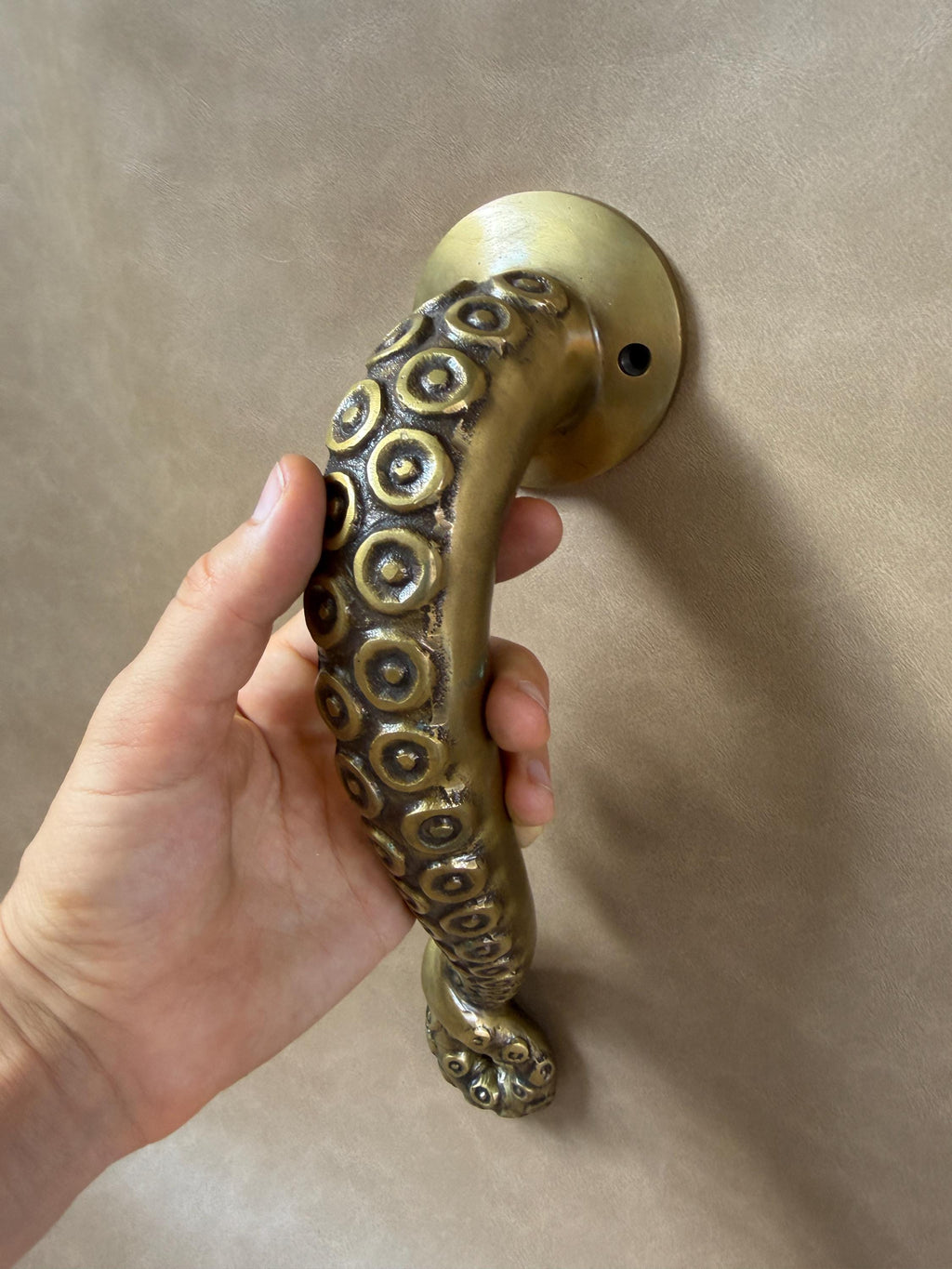 Close-up of a hand gripping the textured brass octopus handle, with suction cups along the curve