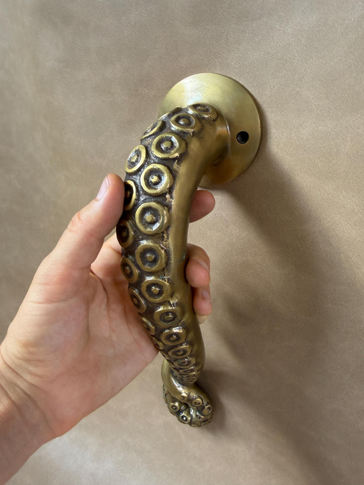 Close-up of a hand gripping the textured brass octopus handle, with suction cups along the curve