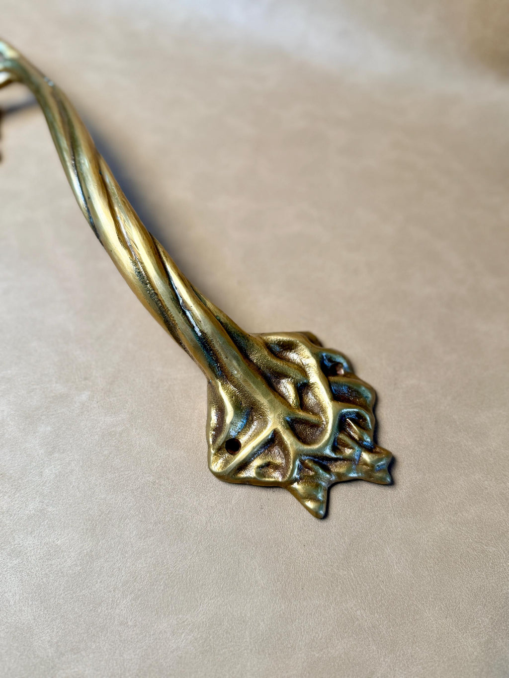 Close-up of the twisted, root-like base of the brass tree handle with screw holes