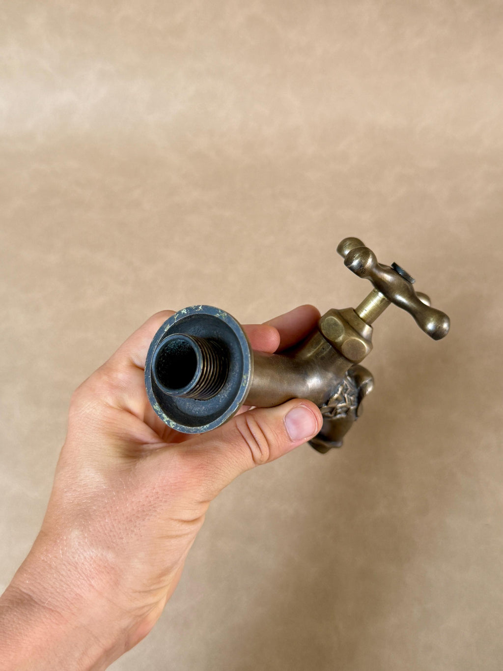 Open threaded connection end of the brass dragon faucet, held in a hand with the cross handle at the top