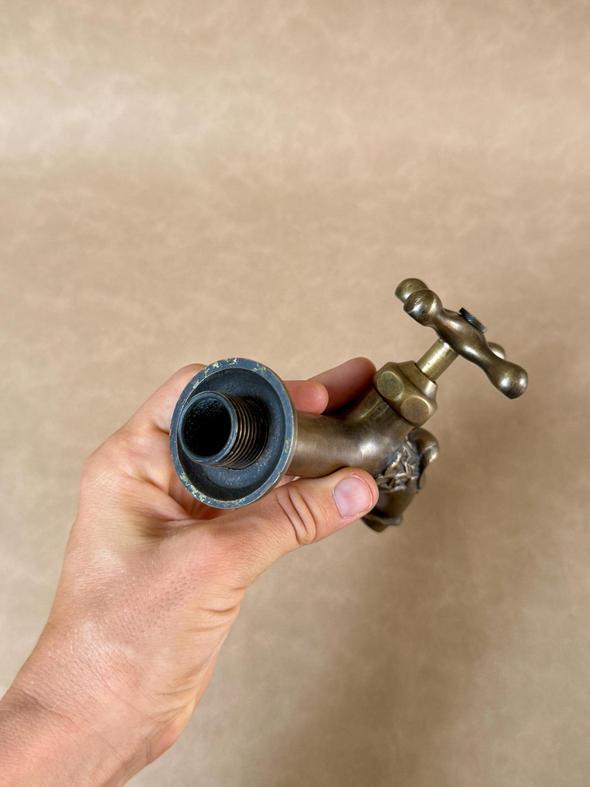 Open threaded connection end of the brass dragon faucet, held in a hand with the cross handle at the top