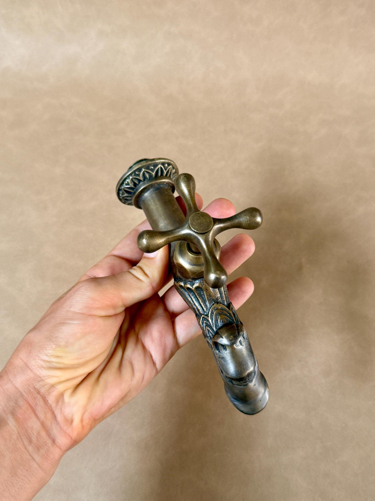 Top view of the brass dragon faucet in a hand, showing the cross handle and dragon head
