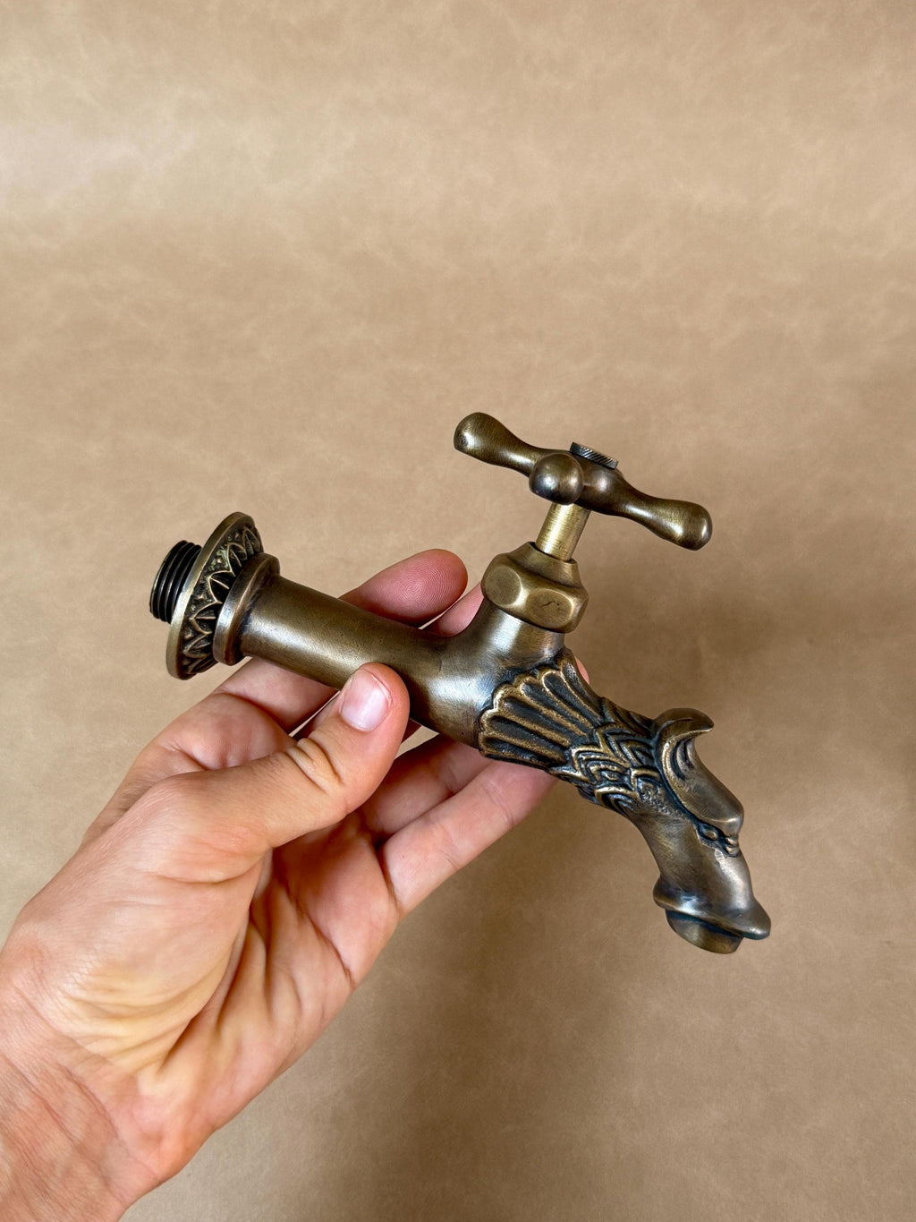 Hand holding the antique brass dragon faucet with its cross handle and scaled dragon head spout