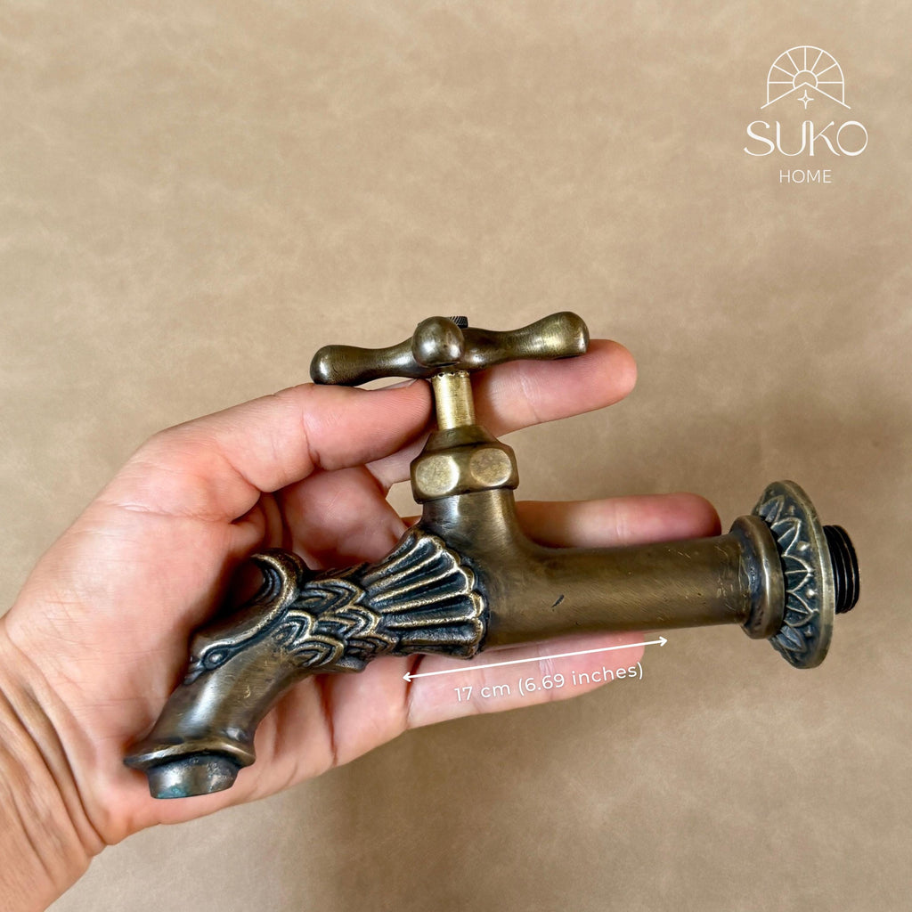 Hand holding the brass dragon faucet horizontally, side view of the scaled dragon head spout