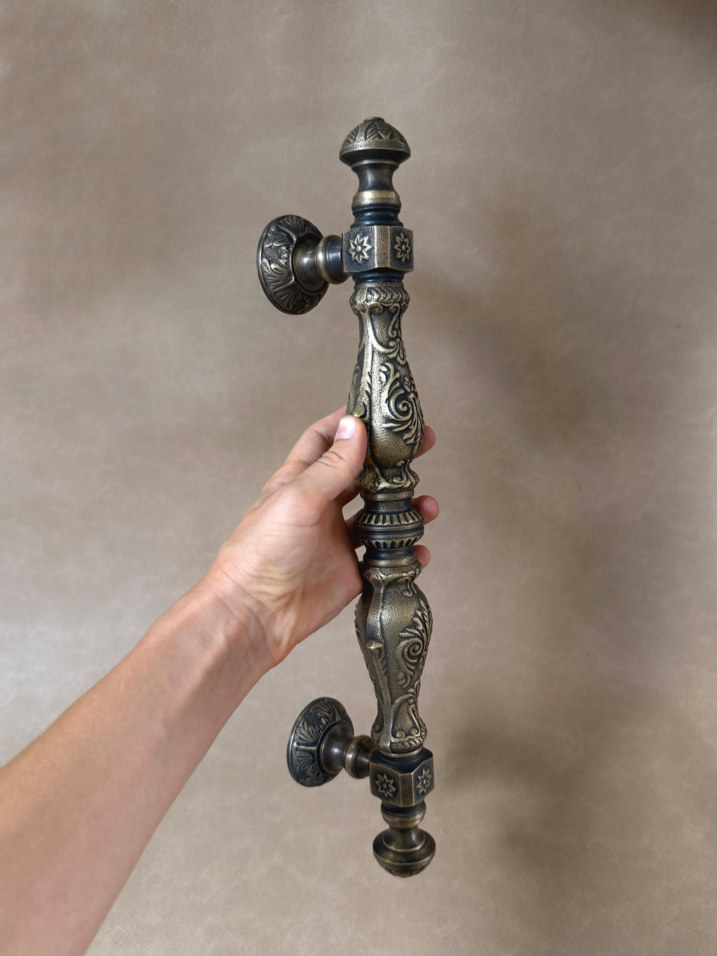 Vertical brass door pull with engraved round mounting plates and an ornate central column