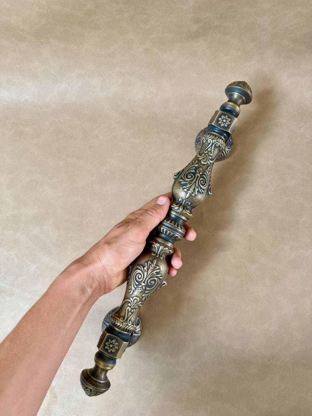 Antique brass door pull with a dark aged finish and raised scrollwork along the shaft