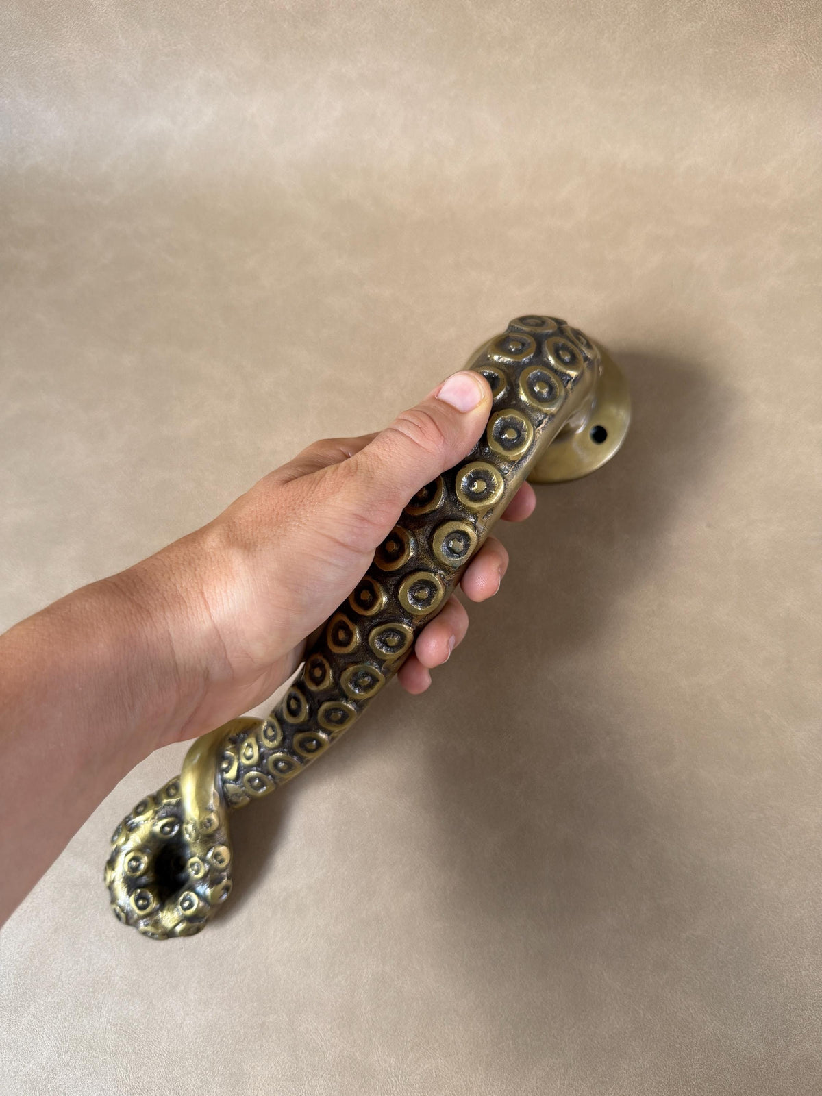 Brass octopus tentacle door handle held in the hand, showing the curled tip