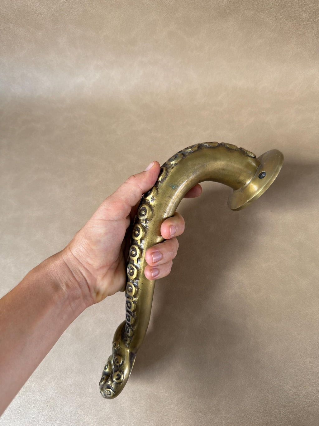 Hand holding the brass octopus tentacle door handle at an angle, with suction cups along its length