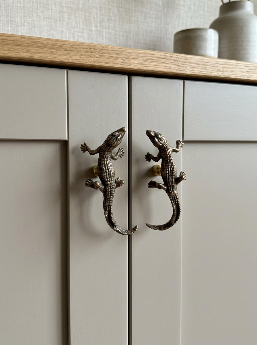 Two brass gecko knobs used as handles on pale gray cabinet doors