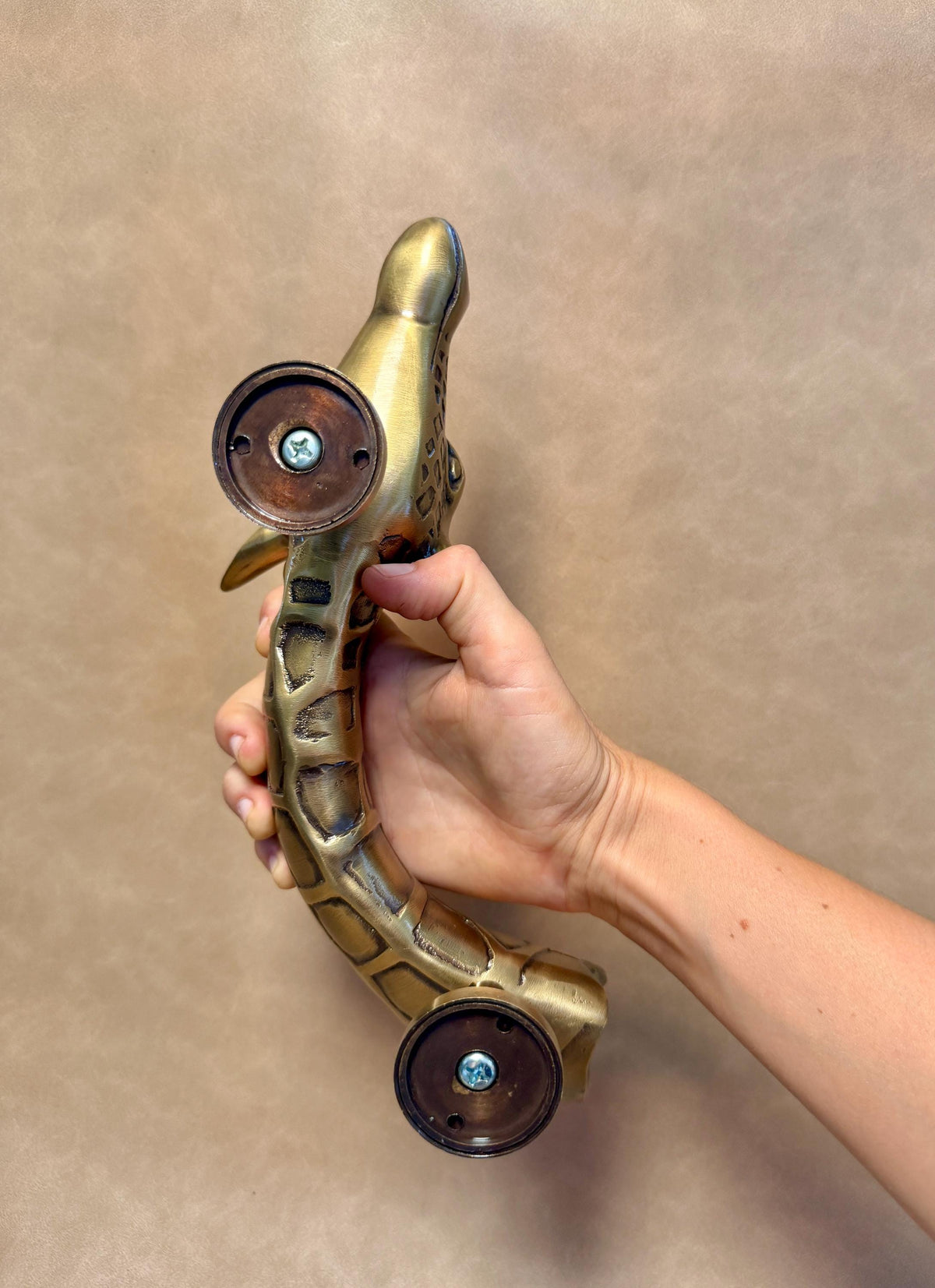 Back of the brass giraffe pull with its two round mounting plates, held in a hand