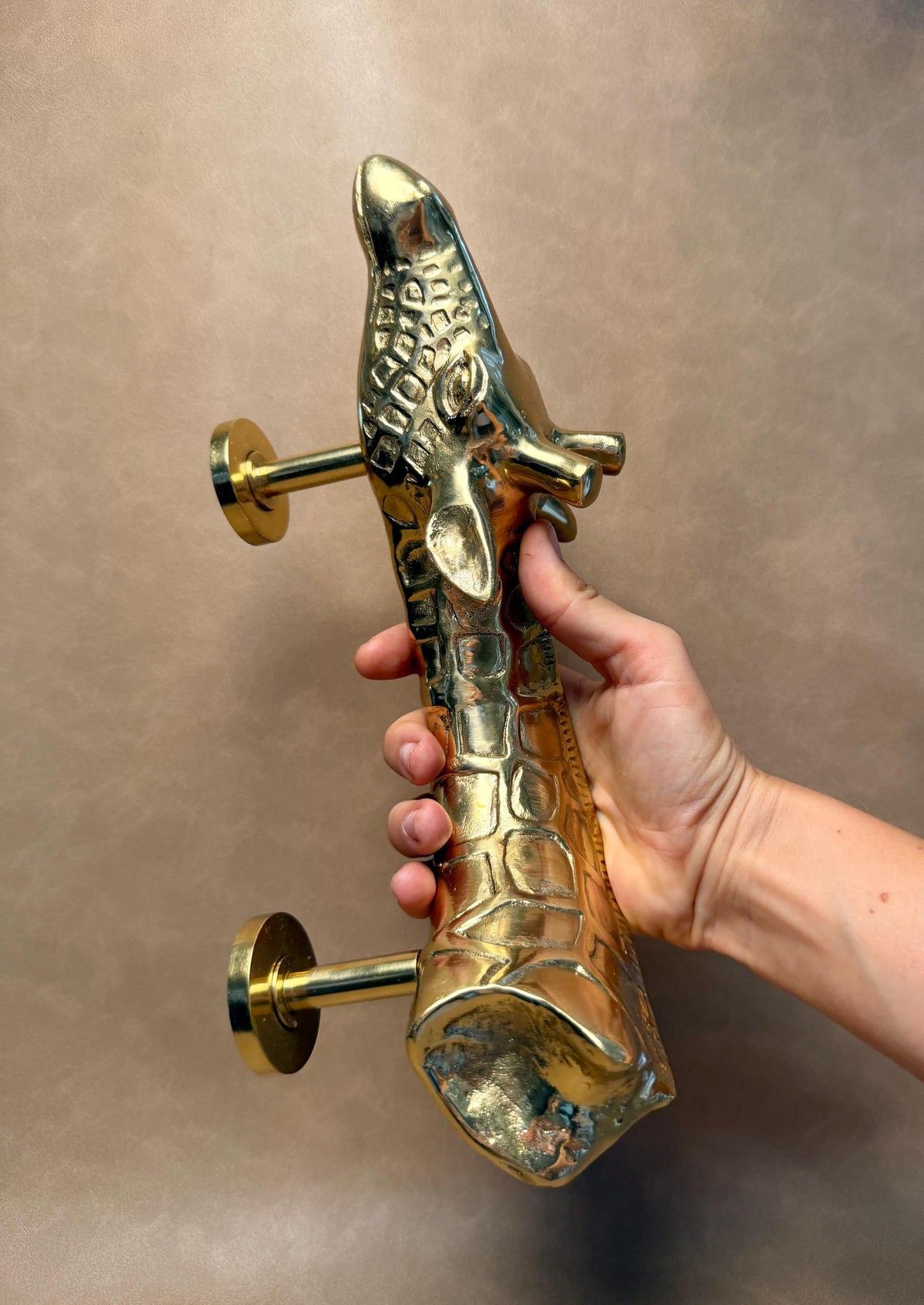 Hand holding the brass giraffe pull in a gold finish, with two mounting posts on the side