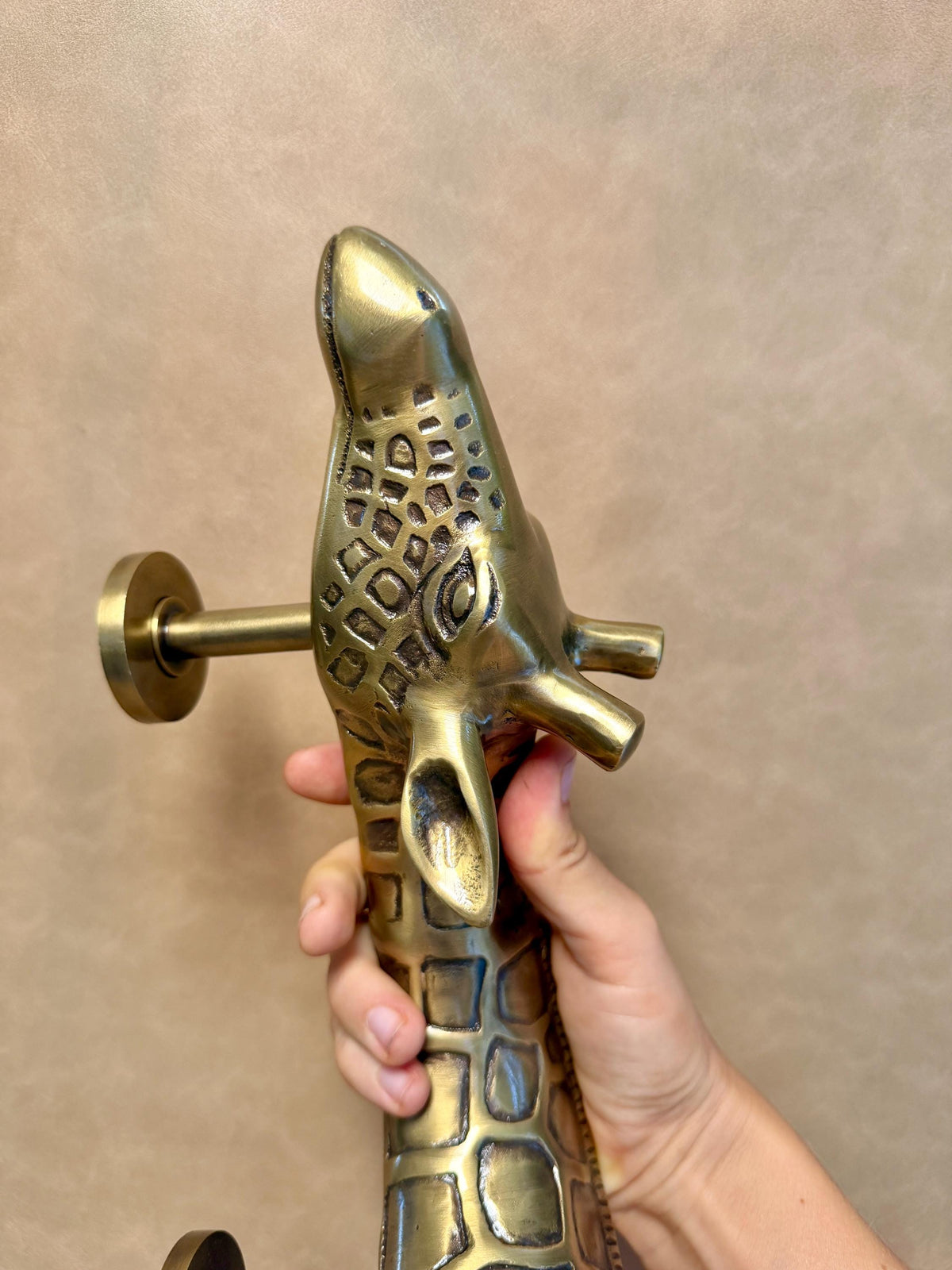 Brass giraffe pull held in a hand, head at the top and two mounting posts on the left