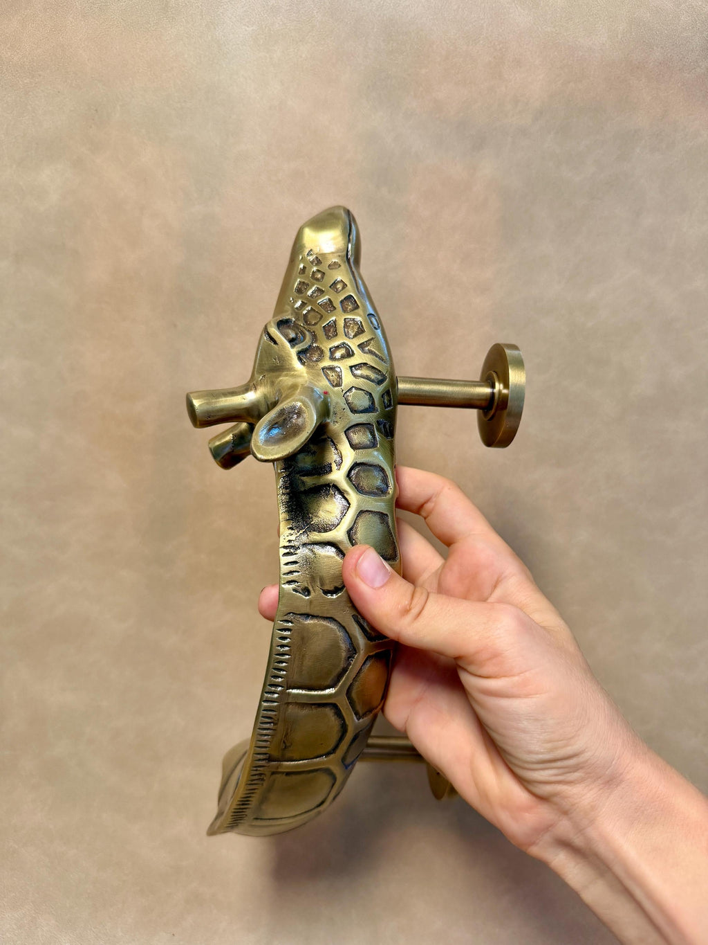 Hand holding the brass giraffe pull at an angle, showing its patterned neck and head
