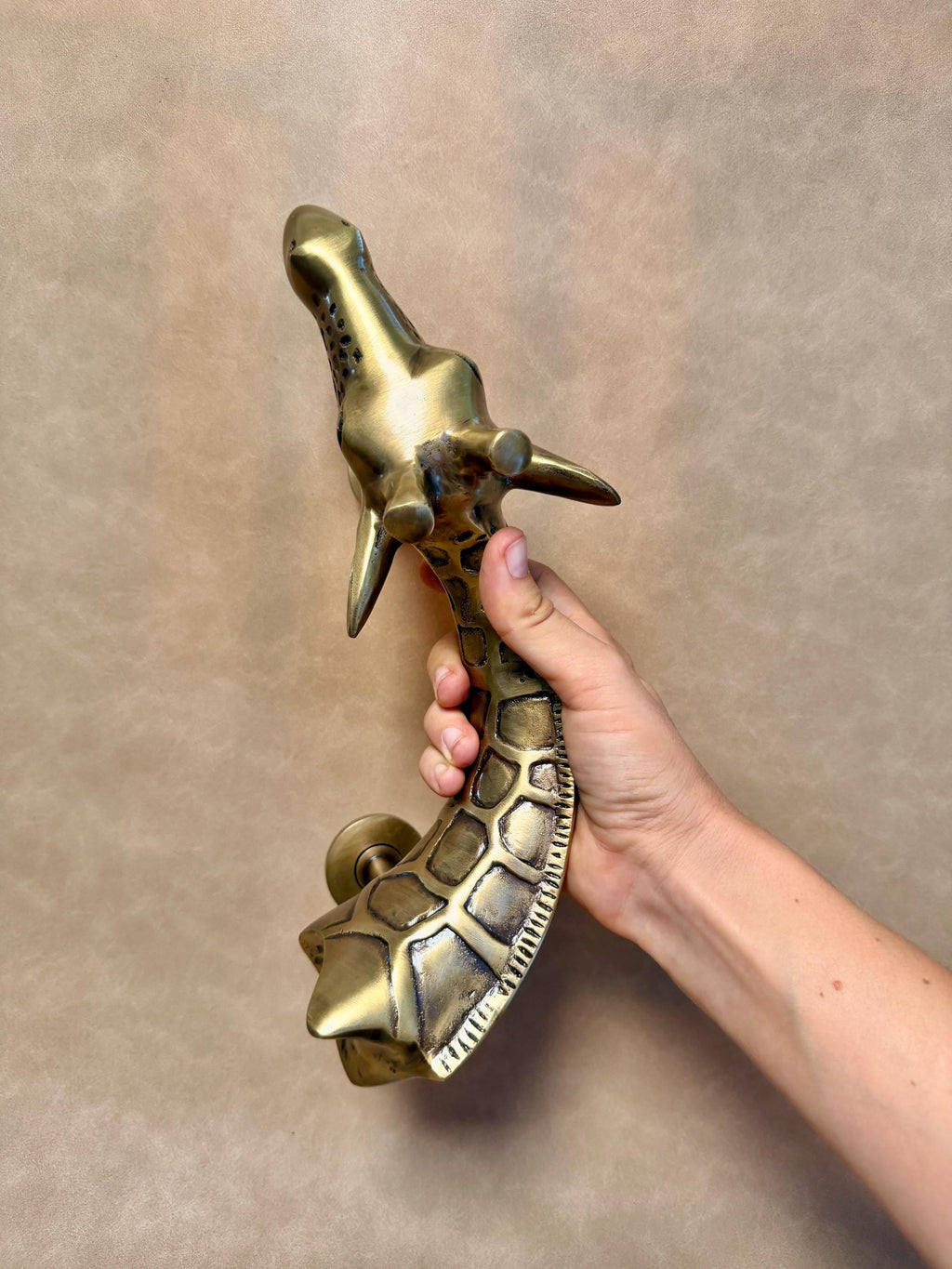 Close view of the giraffe head and the textured neck of the brass pull held in a hand