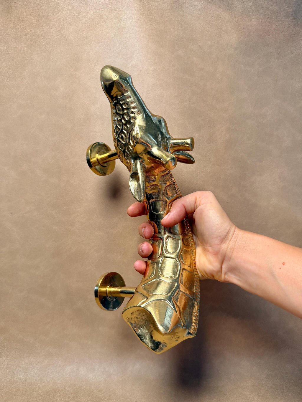 Golden brass giraffe pull held in a hand with both mounting posts visible