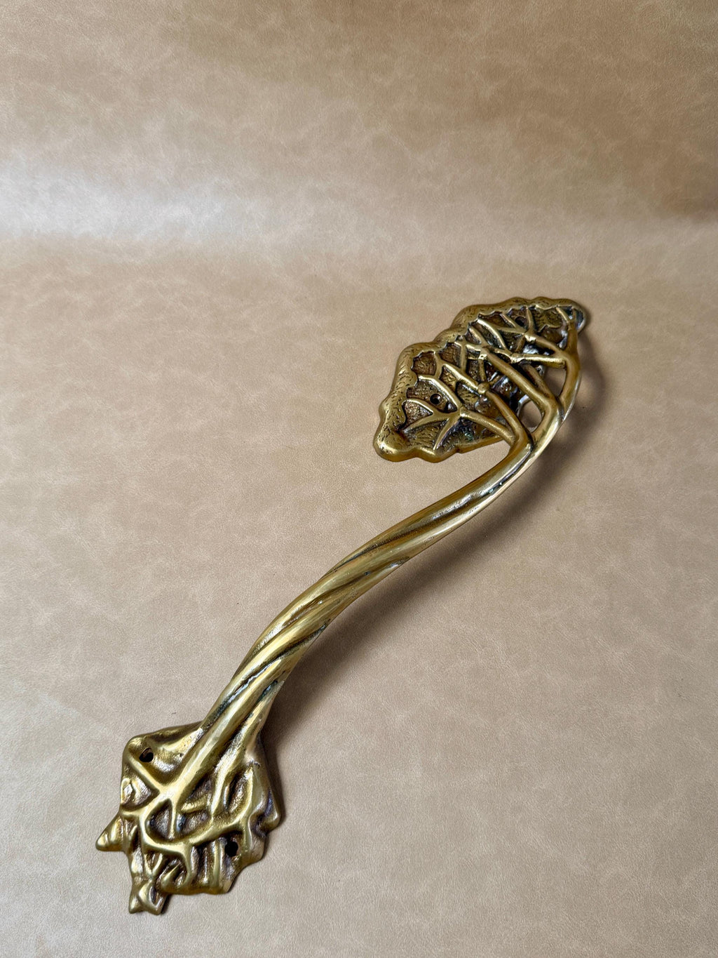 Single brass tree branch door handle with a leafy top and a root-like twisted base on a beige background