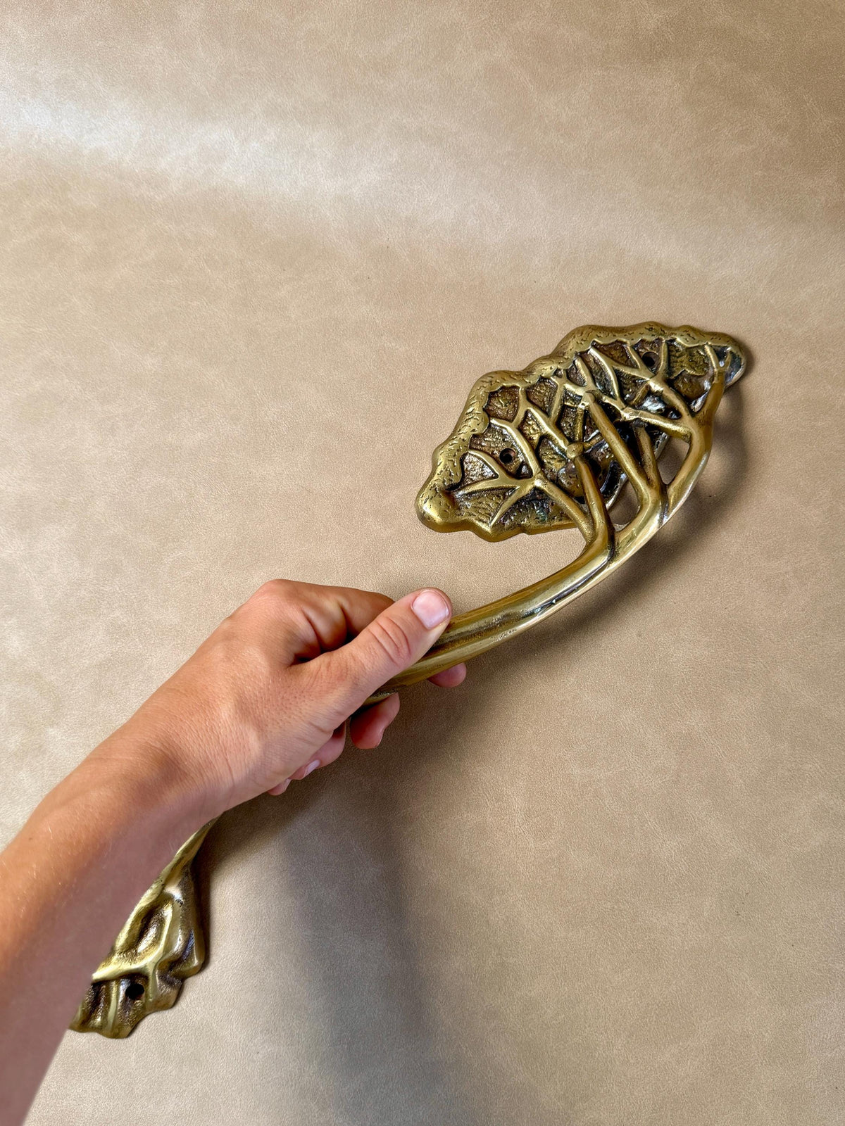 Hand holding the brass tree branch handle at an angle, showing the twisted stem and leaf canopy
