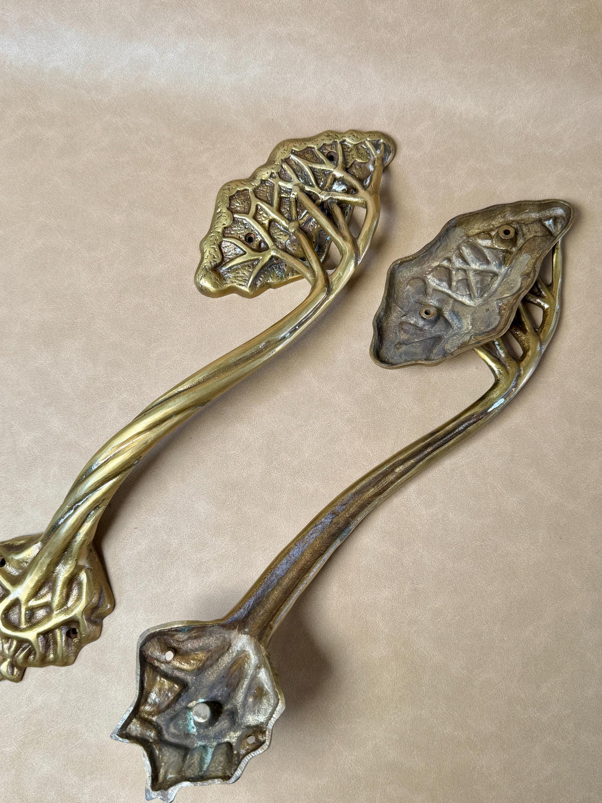 Two brass tree handles, one turned to show the plain silver-toned back of its leaf plate