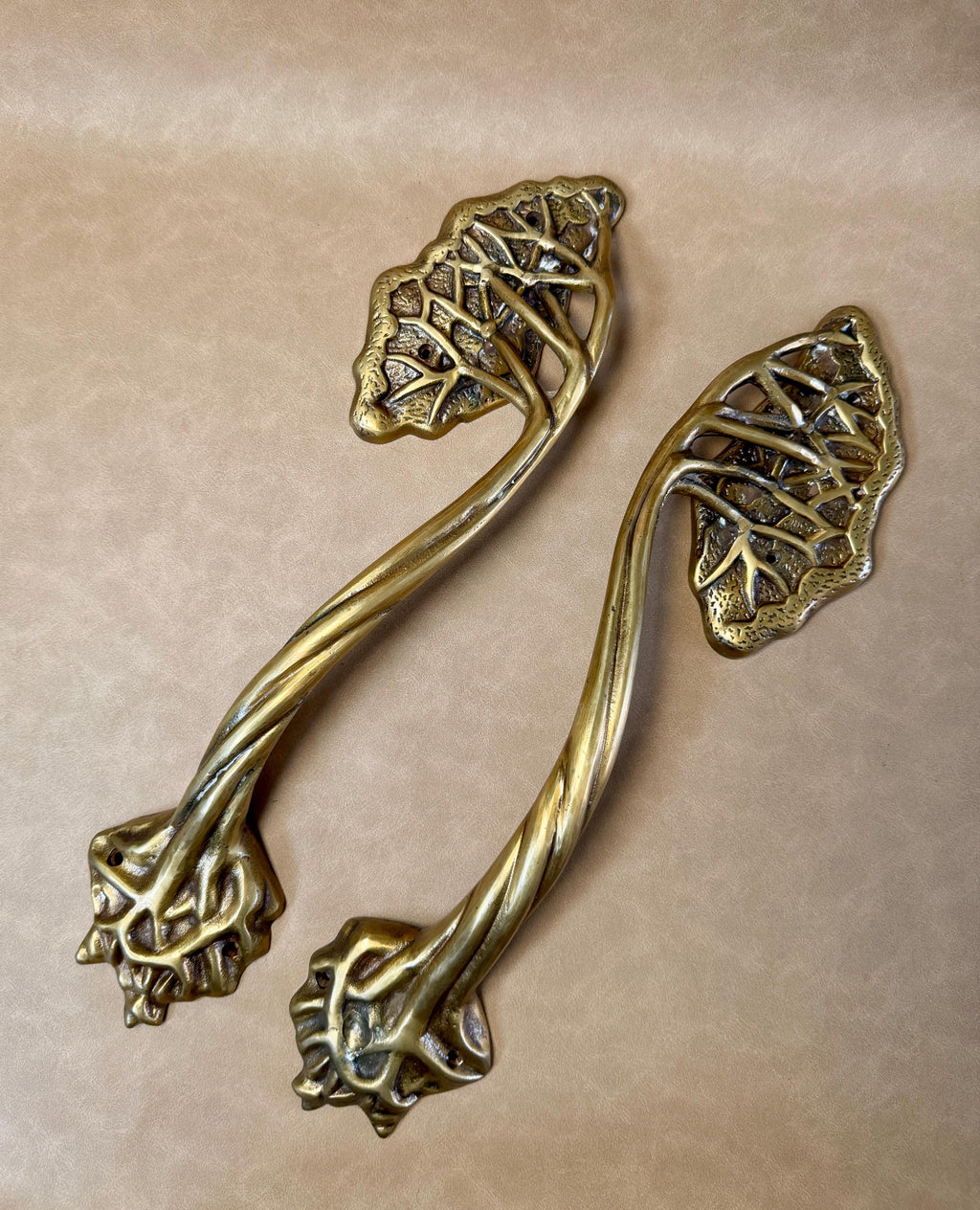 Two brass tree branch door handles lying side by side on a beige background