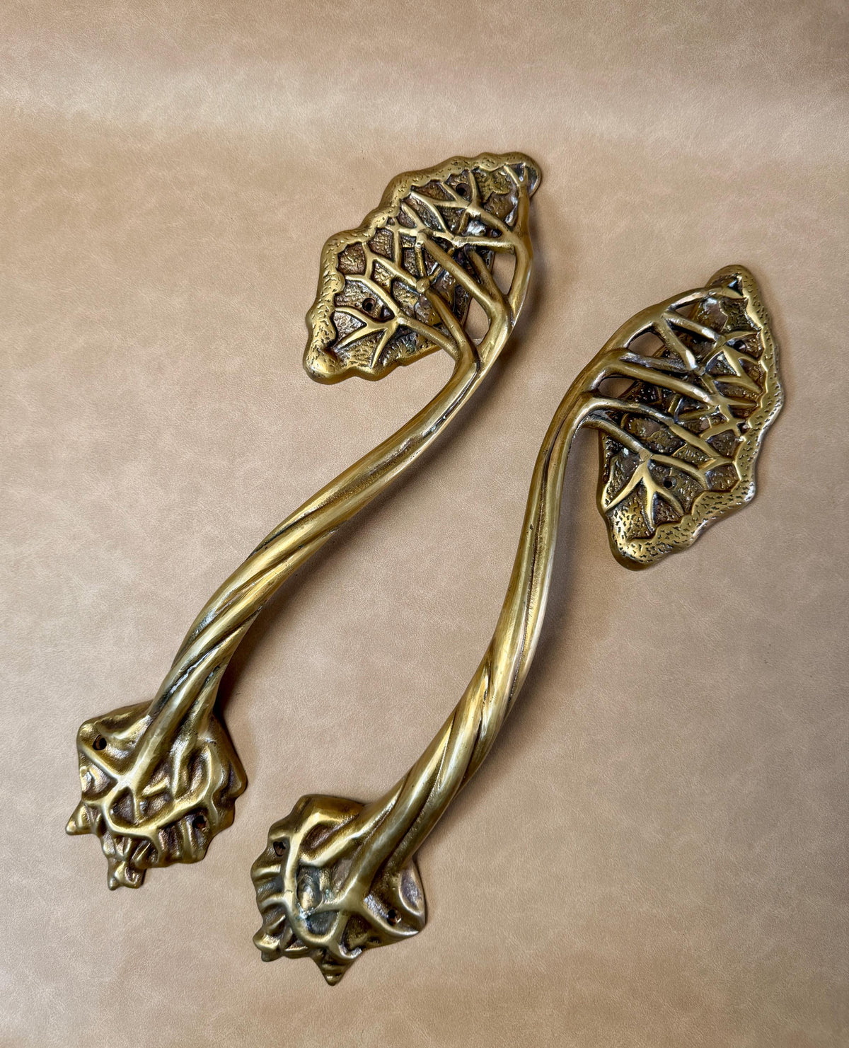 Two brass tree branch door handles lying side by side on a beige background