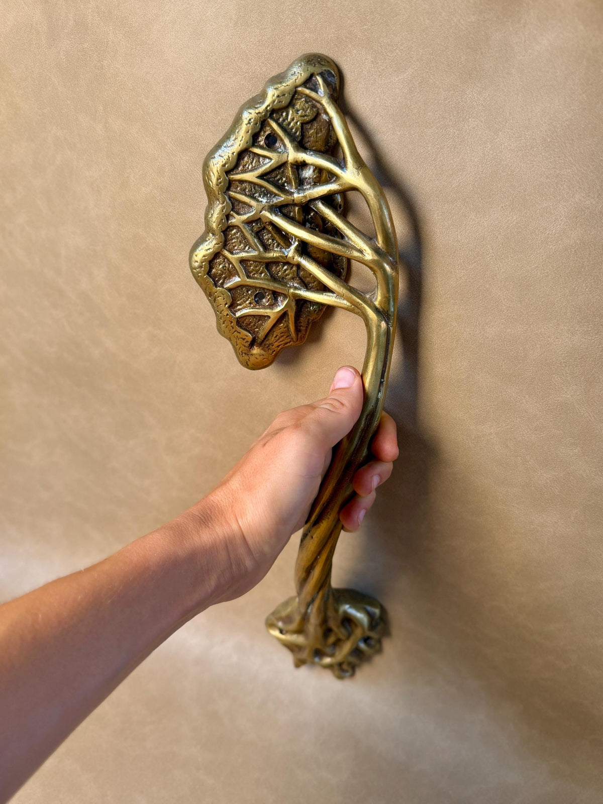 Hand holding the brass tree branch handle upright by its twisted stem, leaf canopy at the top