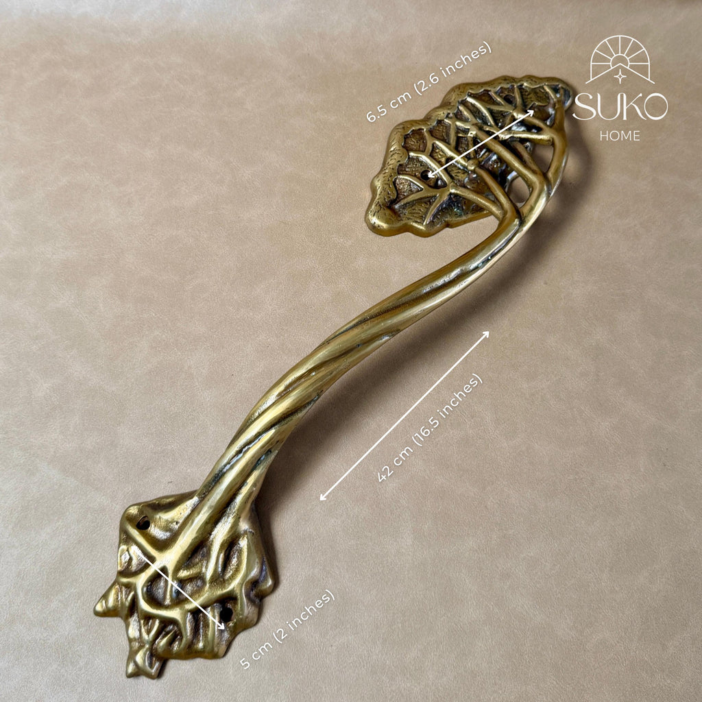 Brass tree branch door handle lying diagonally on a beige background, with a size marker showing its length