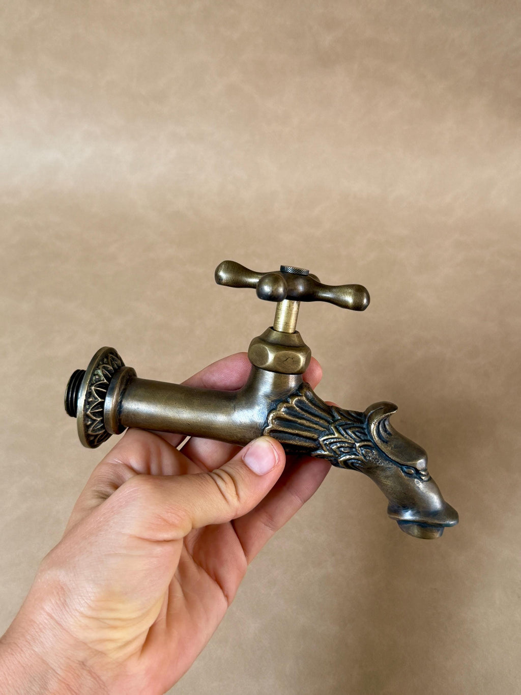 Brass dragon faucet held in a hand, front view with the round flange and cross handle