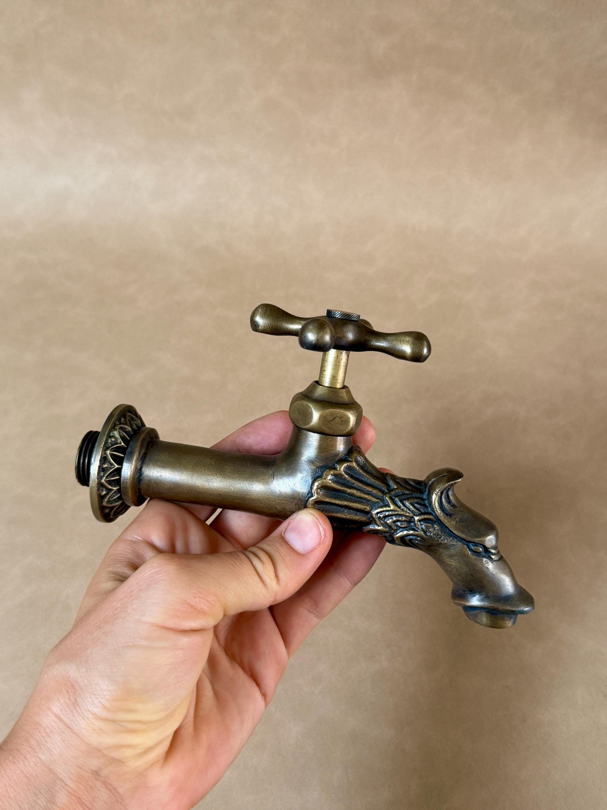 Brass dragon faucet held in a hand, front view with the round flange and cross handle