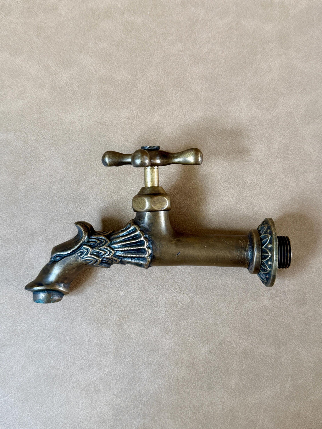 Antique brass dragon faucet lying flat on a beige surface, showing the dragon head spout and round flange