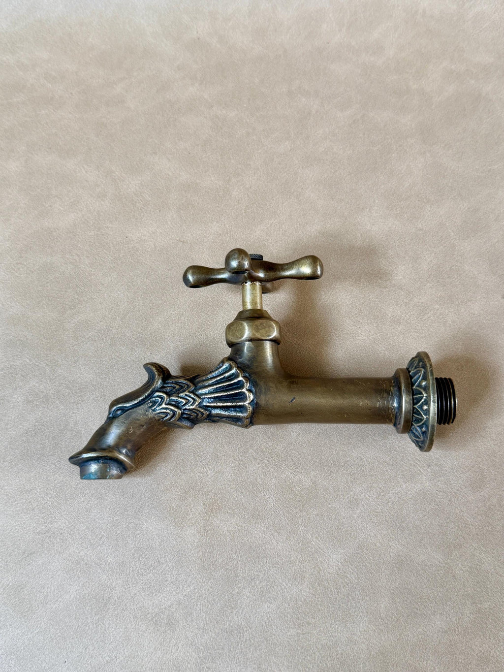 Brass dragon faucet lying on a grey-beige surface, side view with the dragon head spout on the left