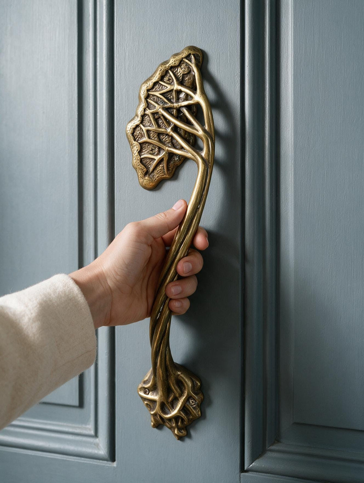 Hand holding the brass tree branch door handle mounted on a blue-gray paneled door