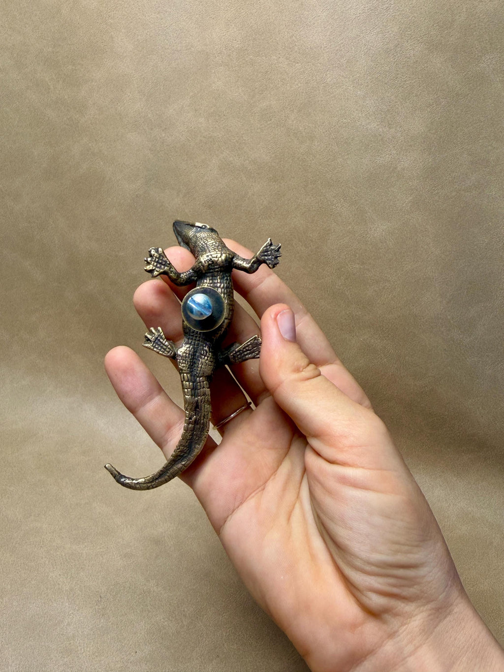 Hand holding an antique brass gecko knob from above, showing its textured scales