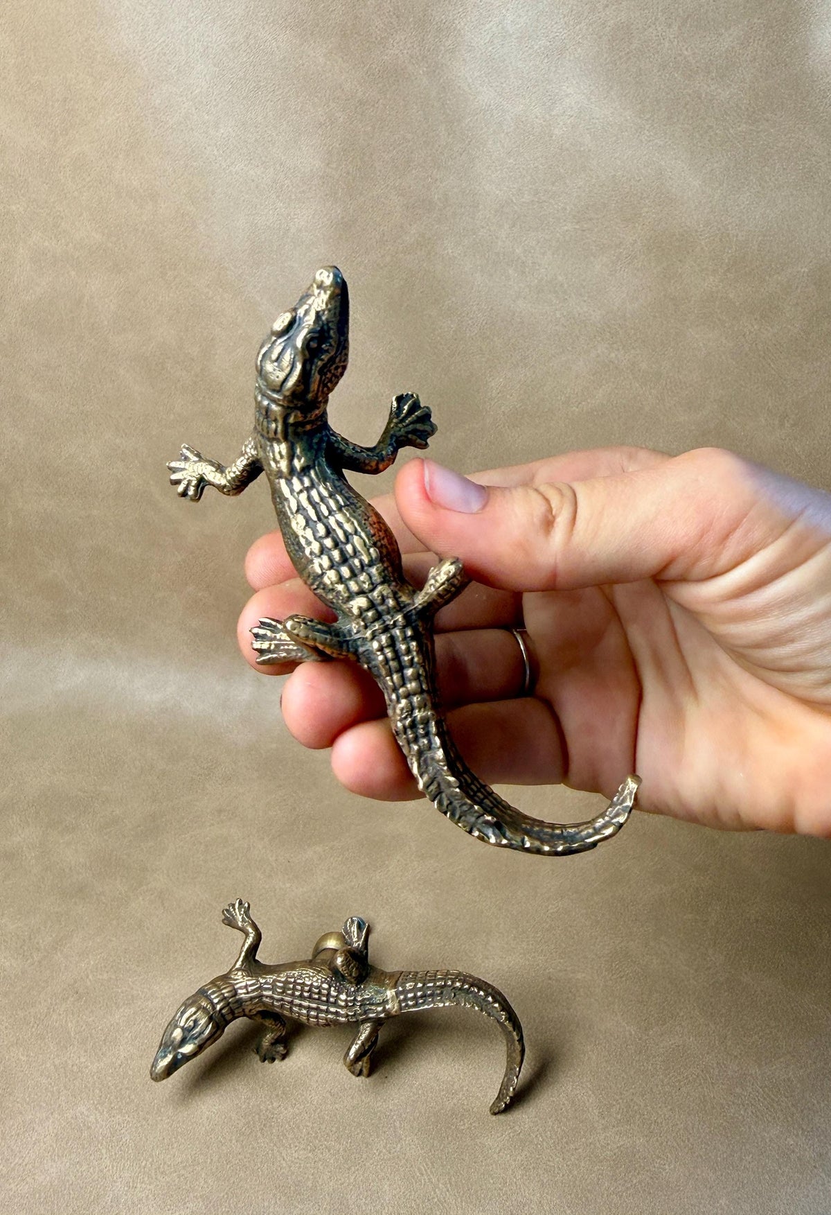 Hand holding an antique-finish brass gecko knob, with a second knob lying below
