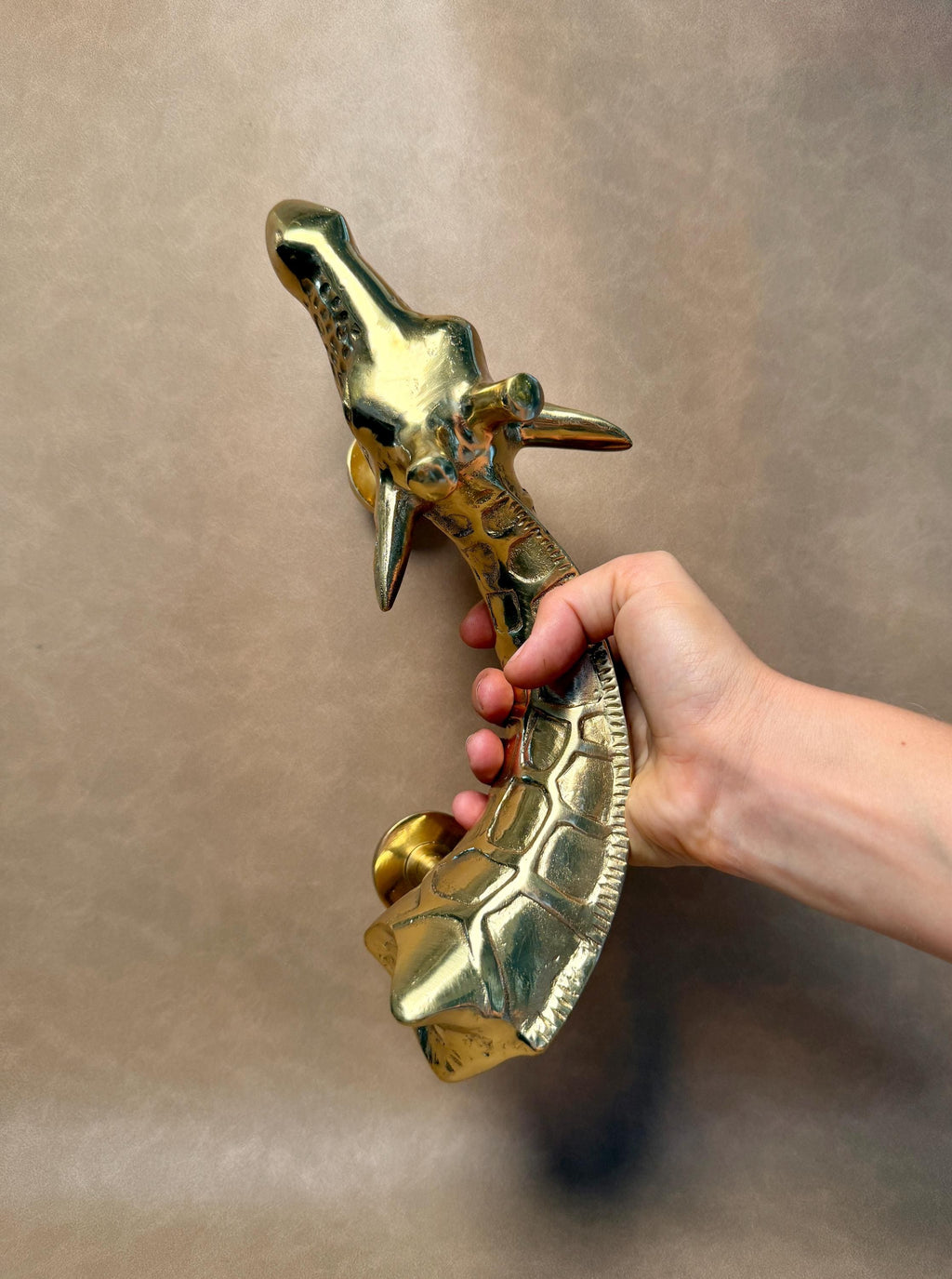 Brass giraffe pull tilted in a hand, showing the head with small horns and the patterned neck