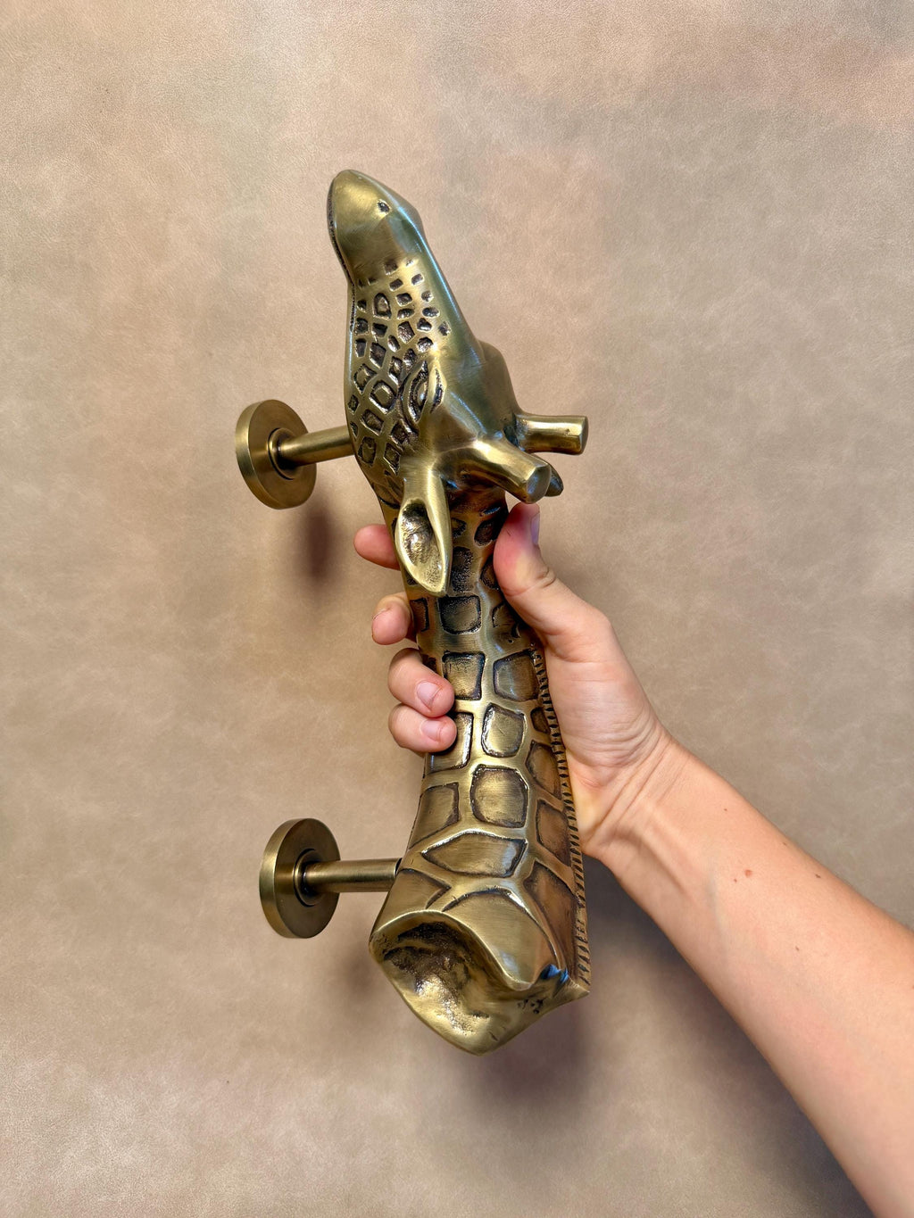 Brass giraffe pull held upright, showing the sculpted head, patterned neck and mounting posts