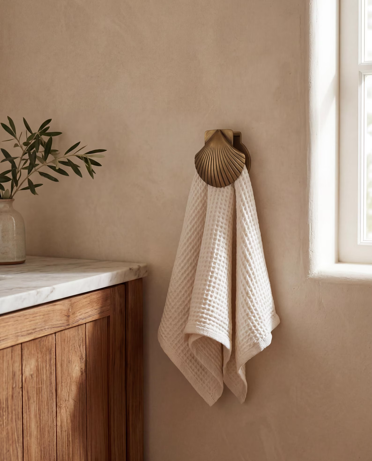 Brass shell clip holding a cream waffle towel beside a bathroom window
